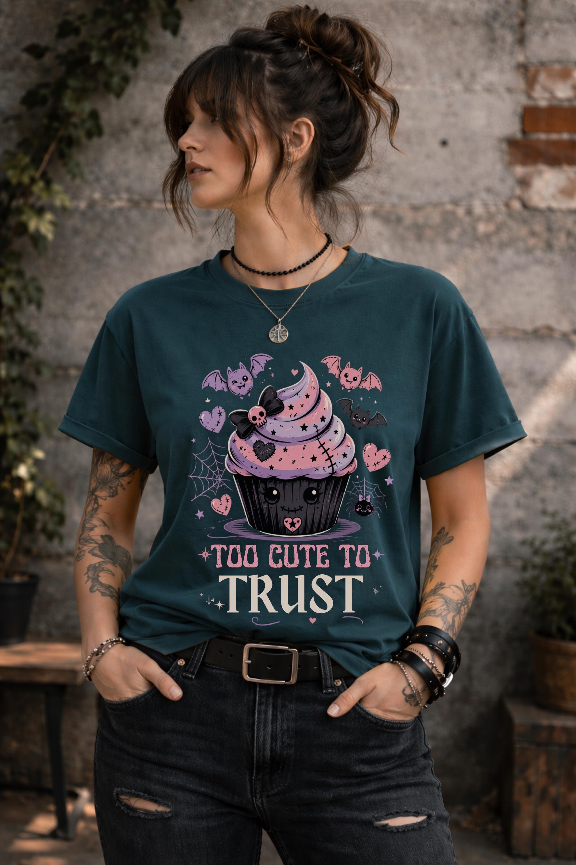 Woman wearing a graphic t-shirt featuring spooky kawaii cupcake with bats hearts spiderwebs and Too Cute to Trust quote