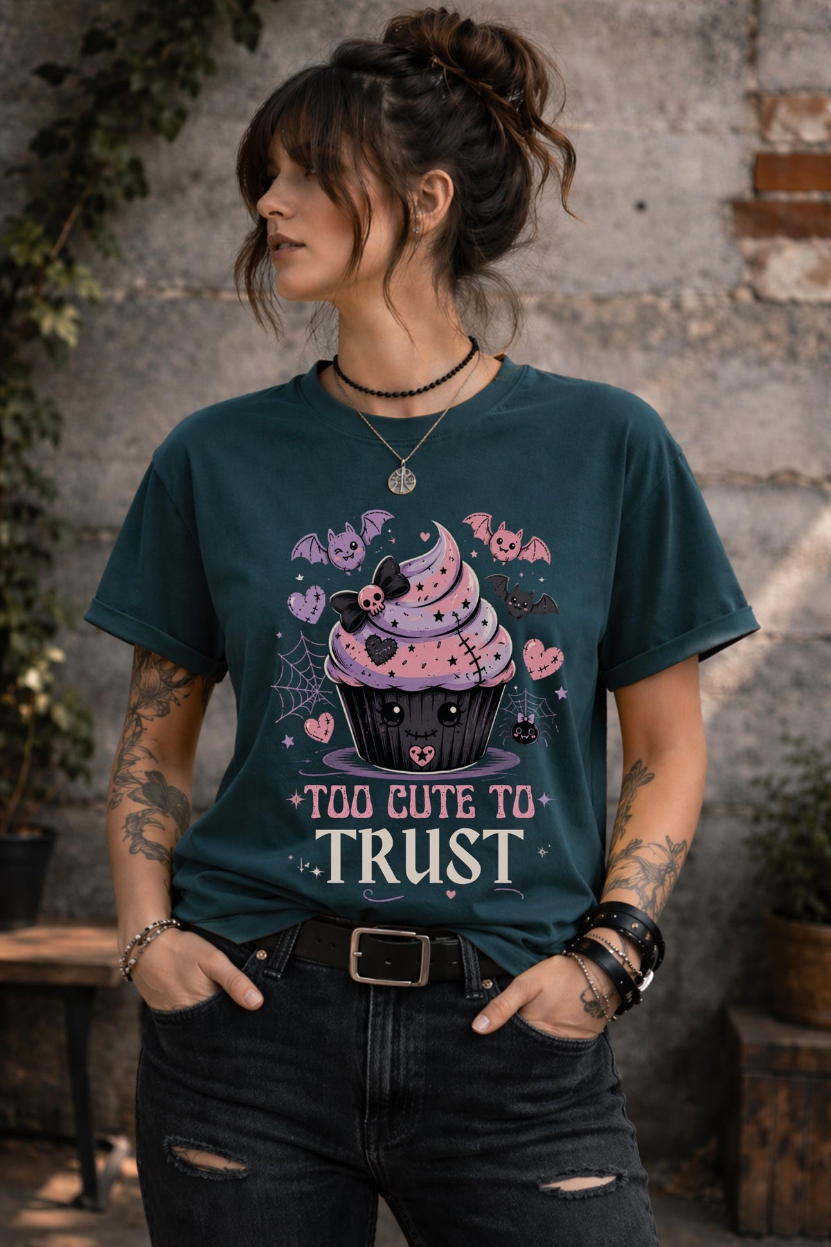 Woman wearing a graphic t-shirt featuring spooky kawaii cupcake with bats hearts spiderwebs and Too Cute to Trust quote