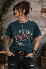 Woman wearing dark vintage wash graphic t-shirt featuring the phrase I Match Energy So Be Careful in distressed typography