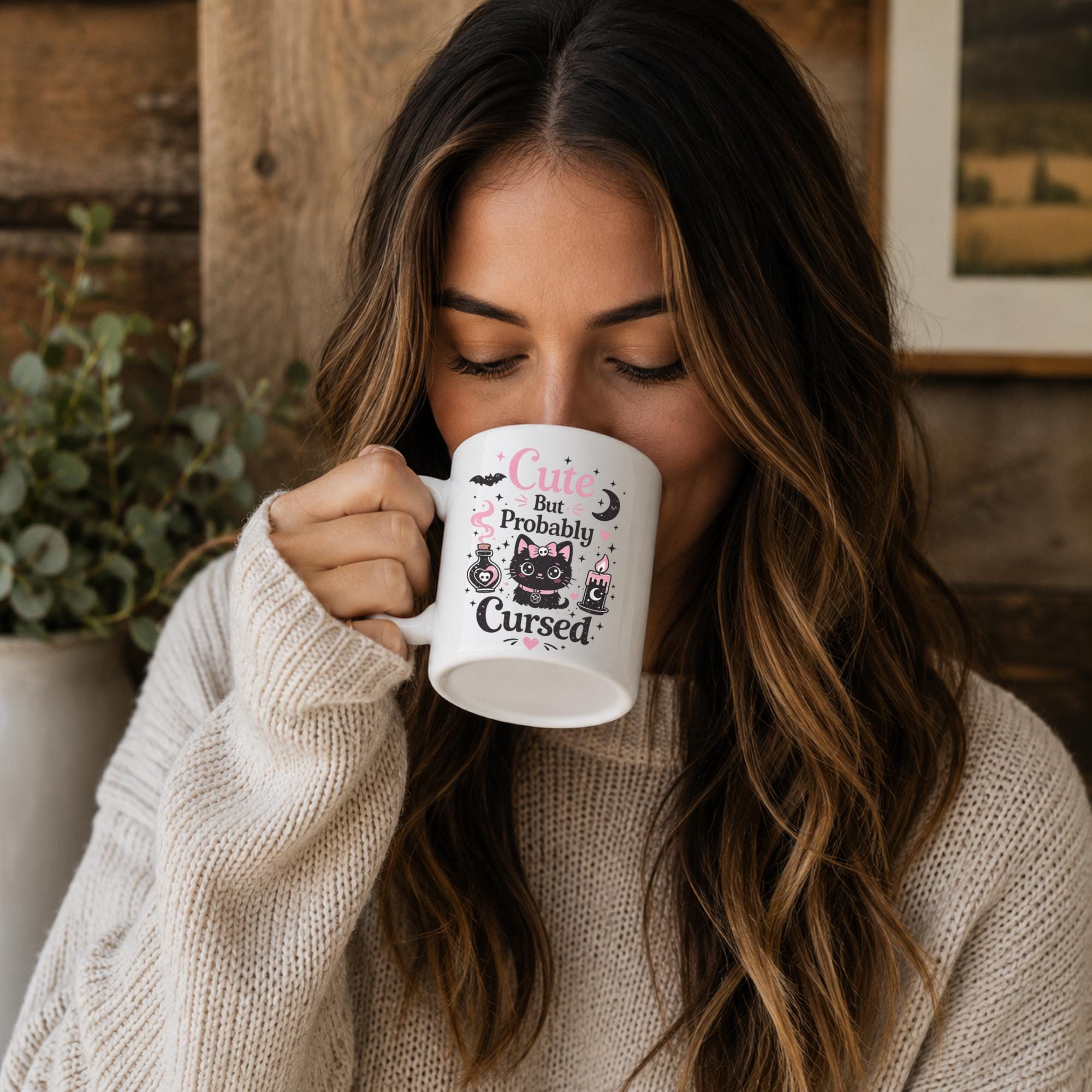 Woman sipping from Cute But Probably Cursed ceramic coffee mug in warm cozy rustic setting