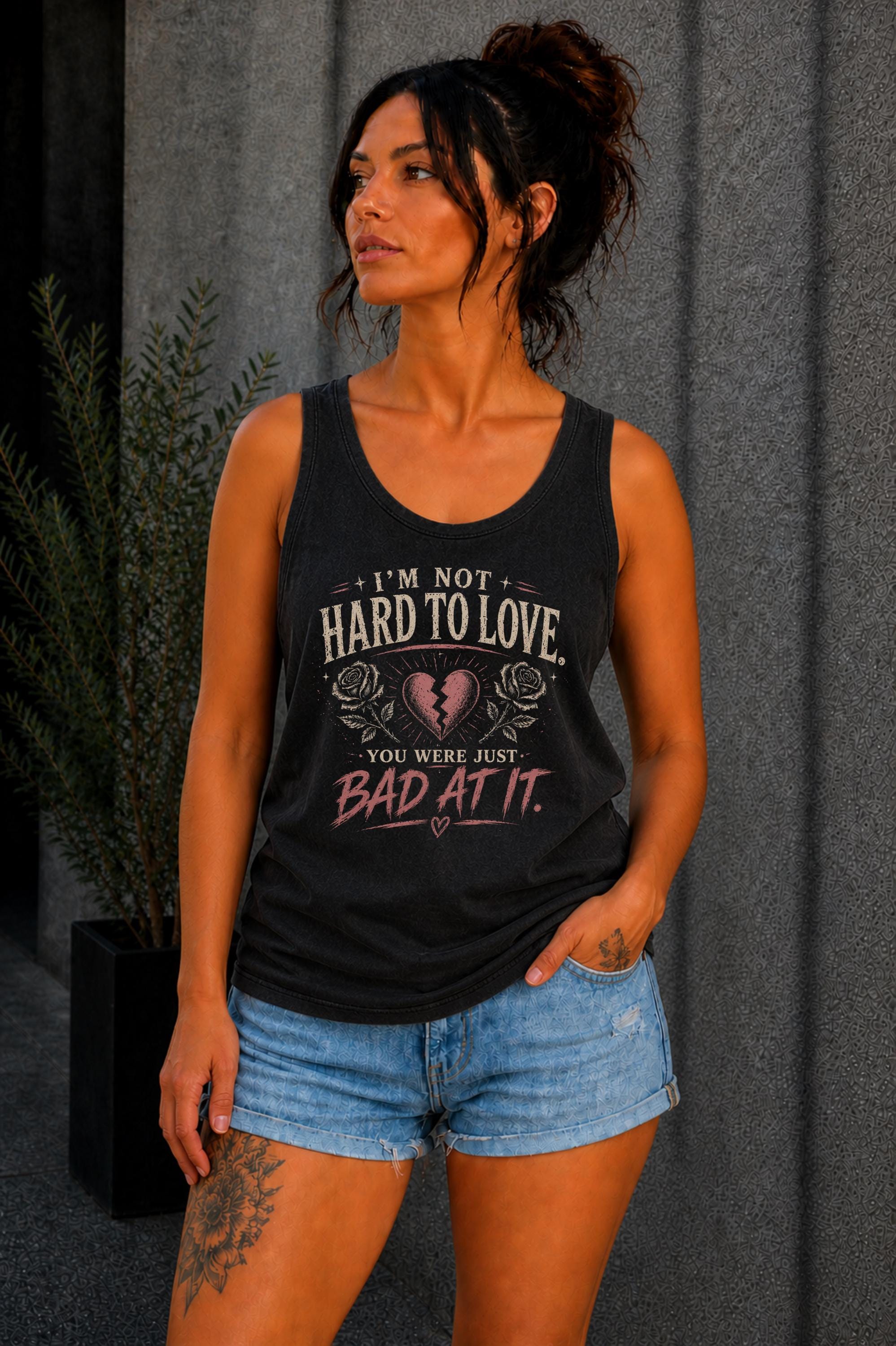 Woman wearing a graphic tank top with sarcastic breakup quote I’m Not Hard to Love You Were Just Bad At It with broken heart design