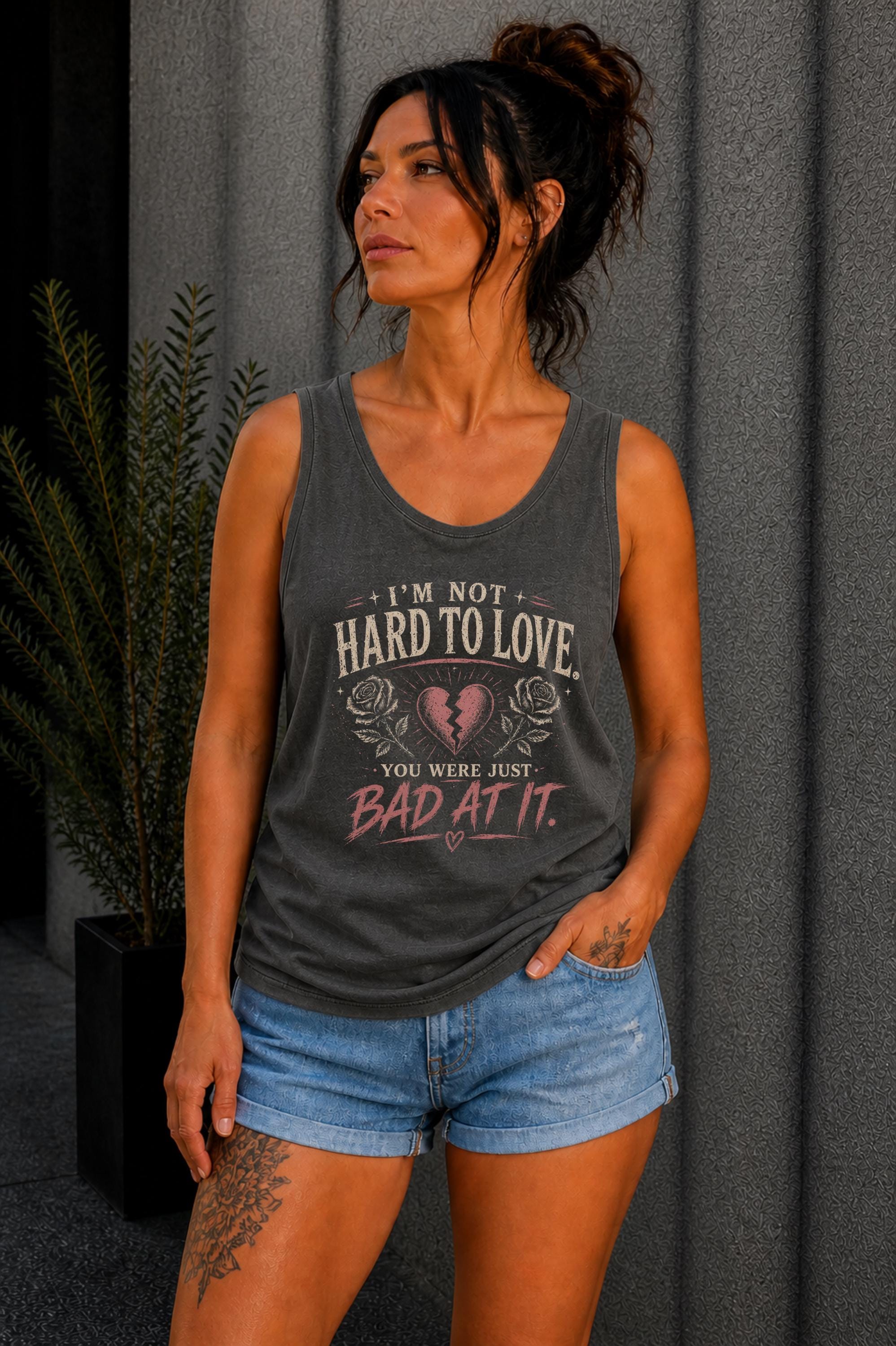 Woman wearing a graphic tank top with sarcastic breakup quote I’m Not Hard to Love You Were Just Bad At It with broken heart design