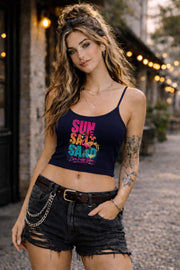 Woman modeling dark crop tank top featuring colorful retro flamingo graphic with Sun Sand Salad Zero Fcks Given summer vacation design against urban industrial background.