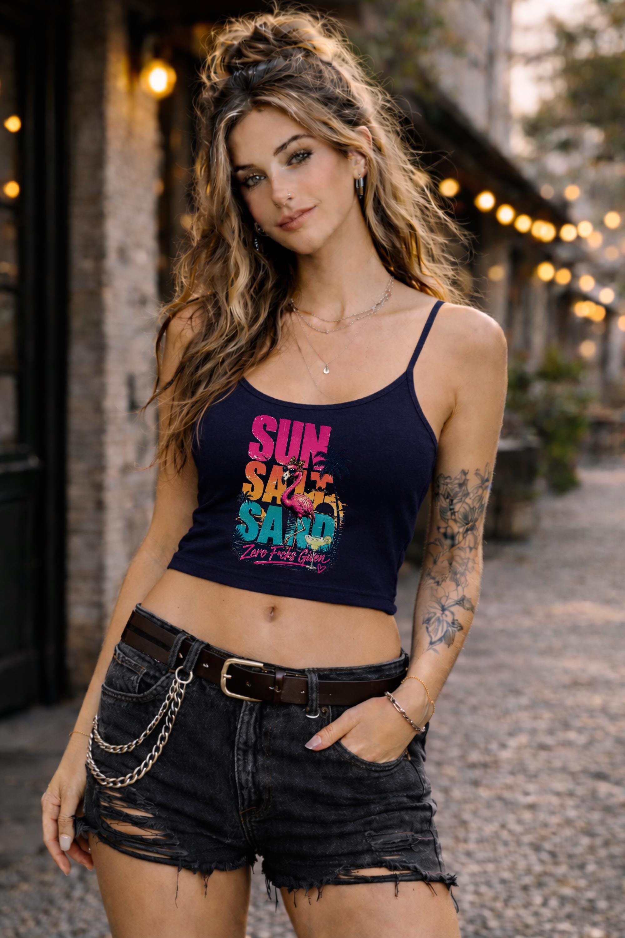 Woman modeling dark crop tank top featuring colorful retro flamingo graphic with Sun Sand Salad Zero Fcks Given summer vacation design against urban industrial background.