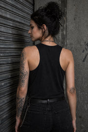 Woman modeling dark crop tank top featuring colorful retro flamingo graphic with Sun Sand Salad Zero Fcks Given summer vacation design against urban industrial background.