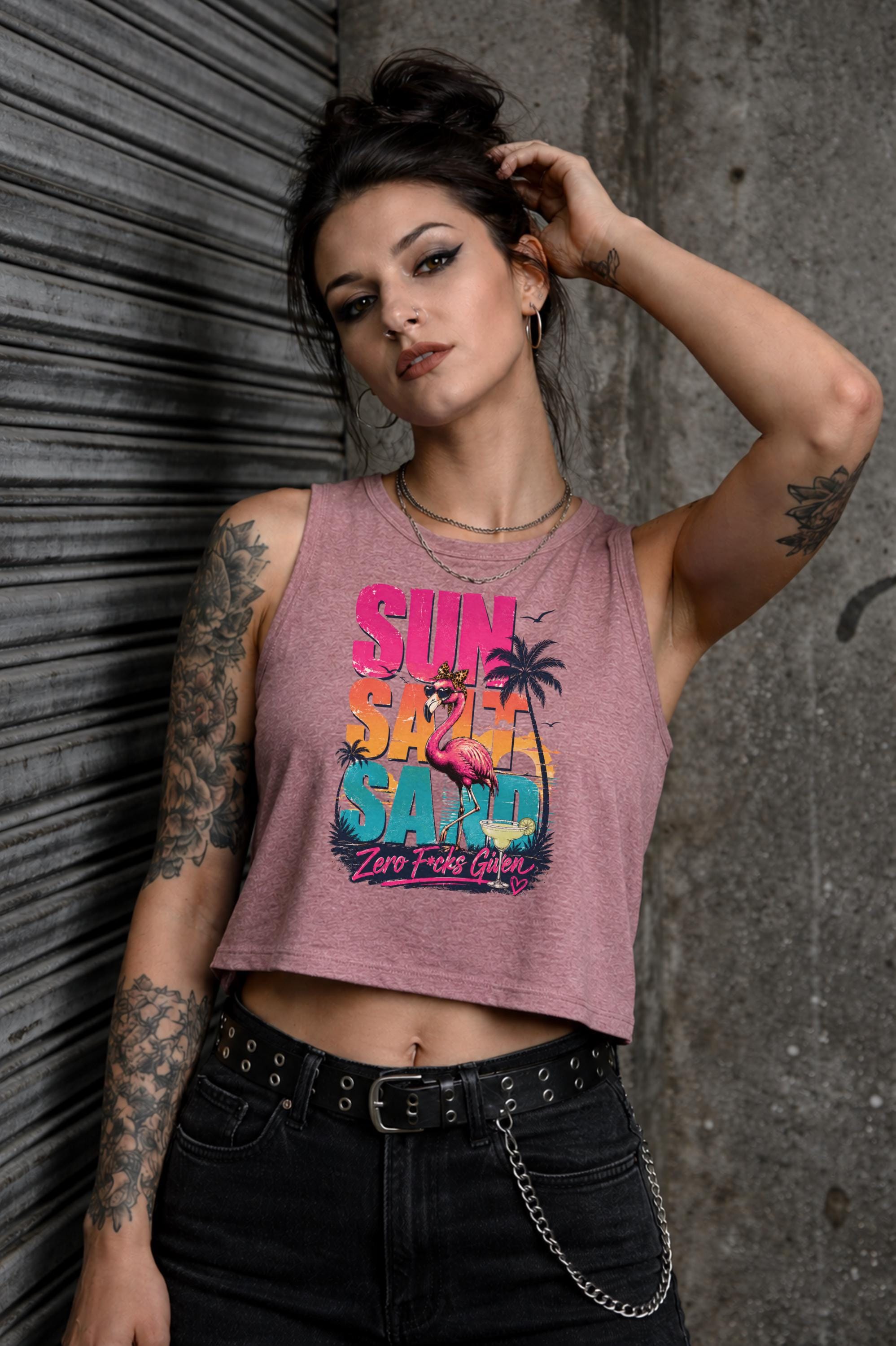 Woman modeling crop tank top featuring colorful retro flamingo graphic with Sun Sand Salad Zero Fcks Given summer vacation design against urban industrial background.