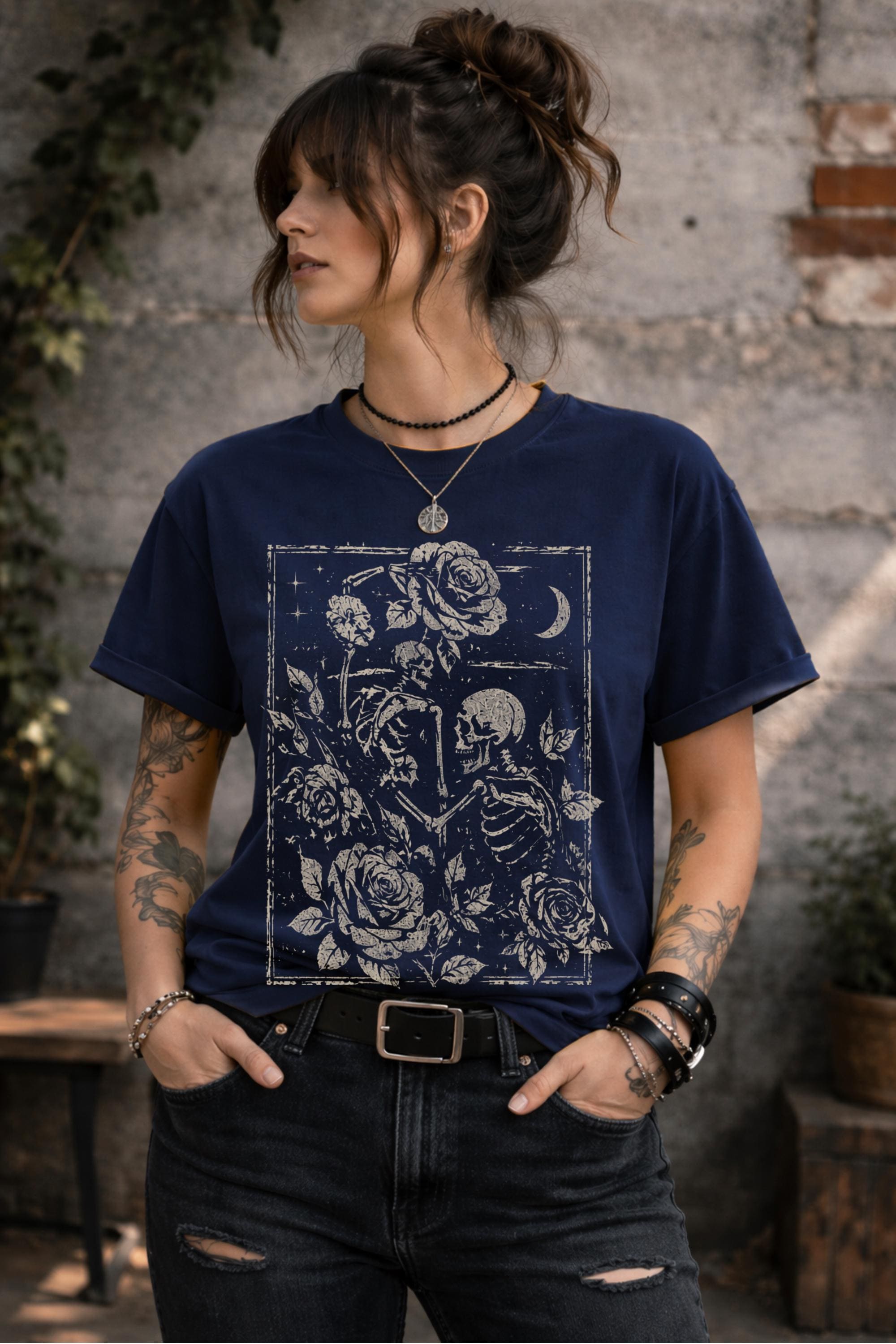 Woman wearing a graphic t-shirt featuring two skeleton lovers surrounded by roses beneath a crescent moon in a gothic dark academia style design.