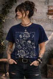 Woman wearing a graphic t-shirt featuring two skeleton lovers surrounded by roses beneath a crescent moon in a gothic dark academia style design.