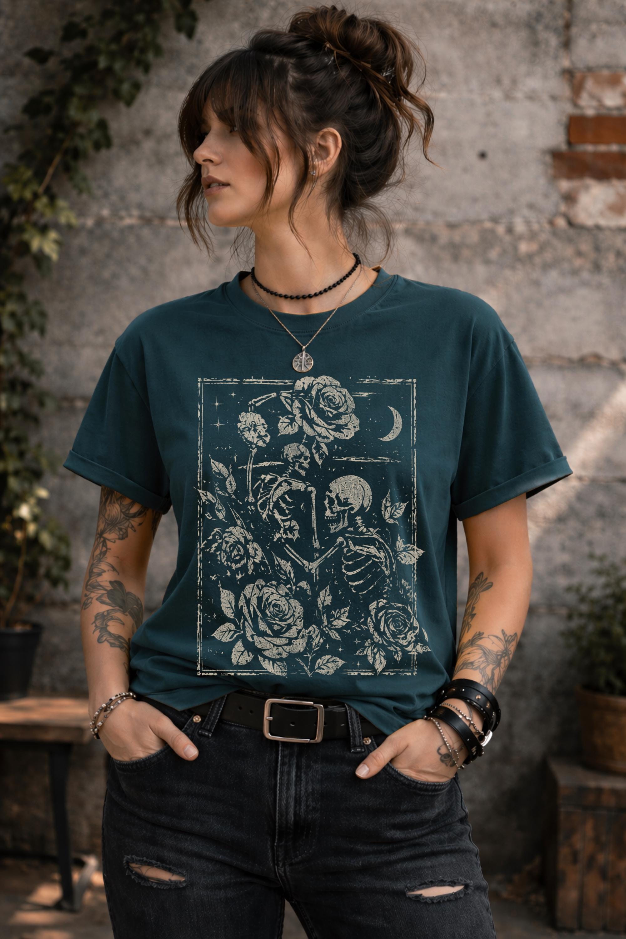 Woman wearing a graphic t-shirt featuring two skeleton lovers surrounded by roses beneath a crescent moon in a gothic dark academia style design.