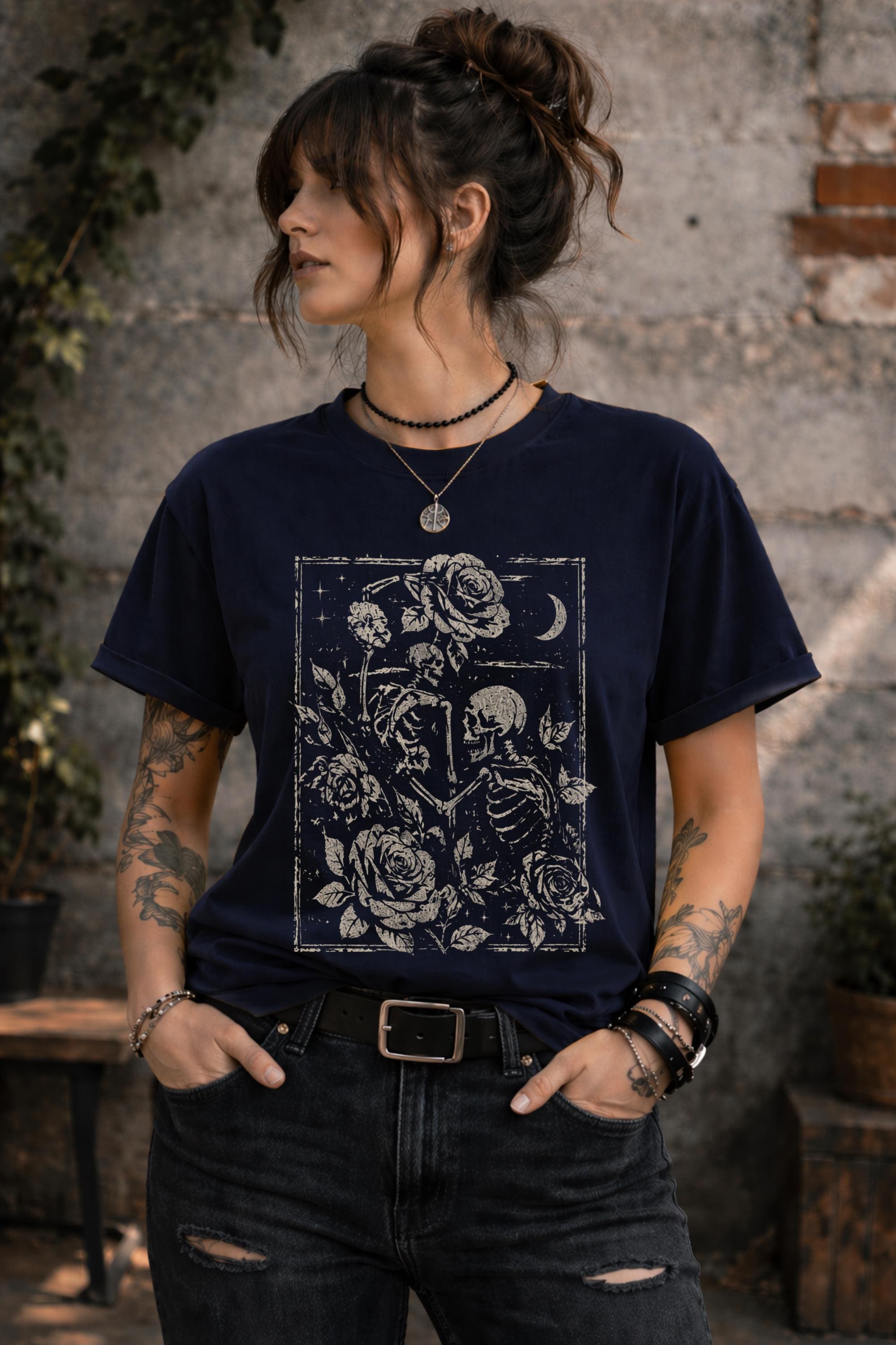 Woman wearing a graphic t-shirt featuring two skeleton lovers surrounded by roses beneath a crescent moon in a gothic dark academia style design.