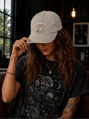 Woman wearing a stone classic dad cap featuring a colorful Bookish Life graphic with stacked books, glasses, and a playful reading-themed illustration.