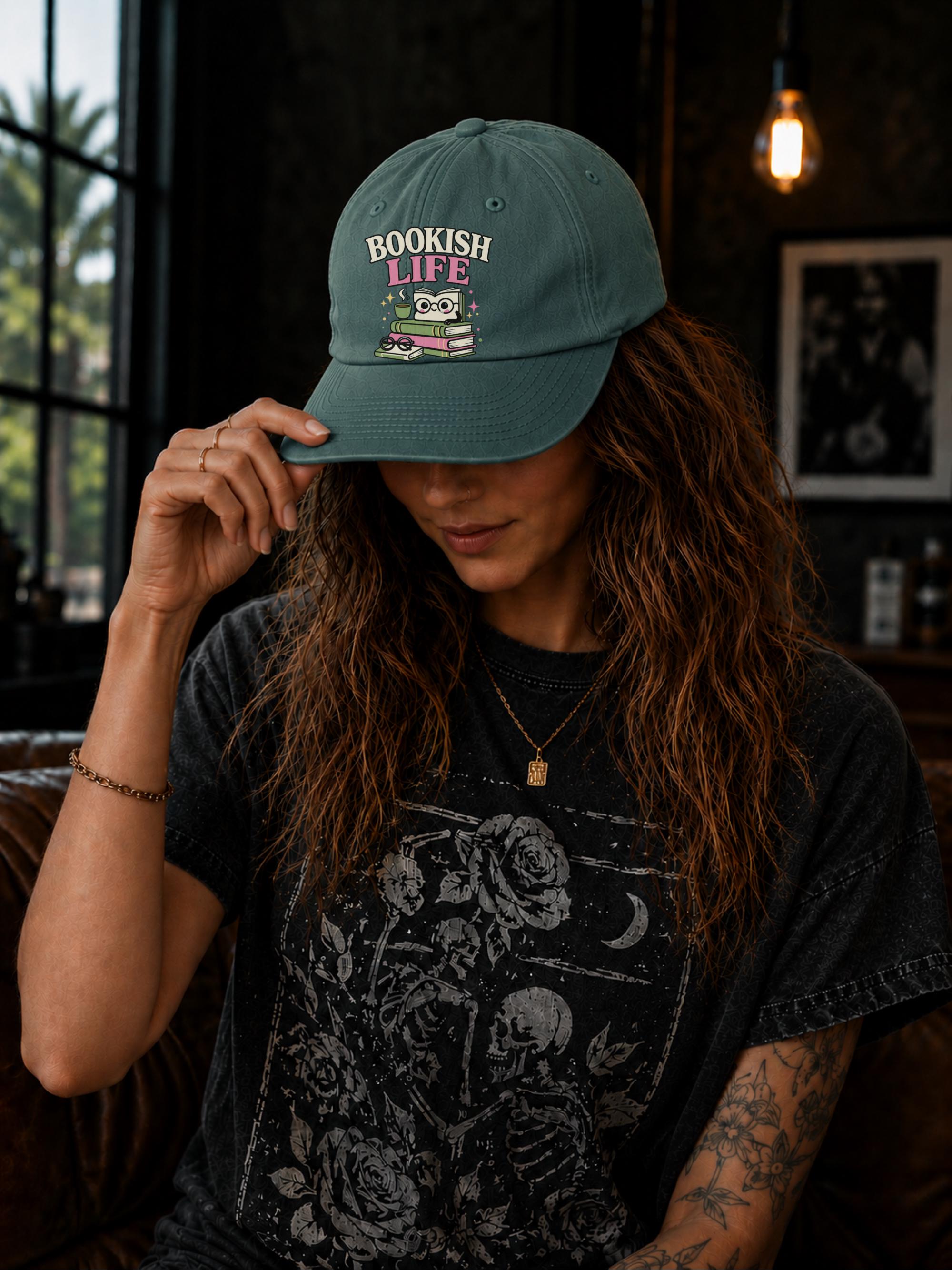 Woman wearing a spruce classic dad cap featuring a colorful Bookish Life graphic with stacked books, glasses, and a playful reading-themed illustration.