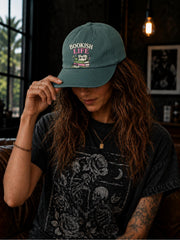 Woman wearing a spruce classic dad cap featuring a colorful Bookish Life graphic with stacked books, glasses, and a playful reading-themed illustration.