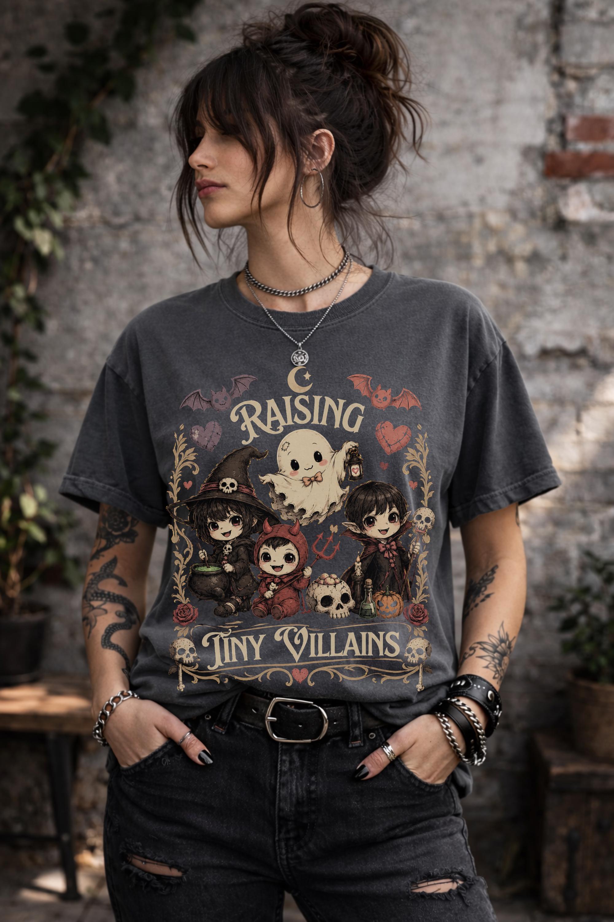 Cute spooky mom tee showcasing Raising Tiny Villains design with magical characters, moon accents, and Halloween-inspired illustrations.