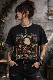 Raising Tiny Villains graphic t-shirt featuring cute ghost, witch, vampire, devil child, bats, skulls, hearts, and spooky gothic artwork.