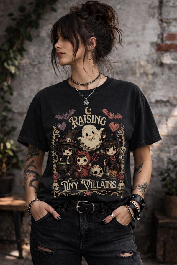 Raising Tiny Villains graphic t-shirt featuring cute ghost, witch, vampire, devil child, bats, skulls, hearts, and spooky gothic artwork.