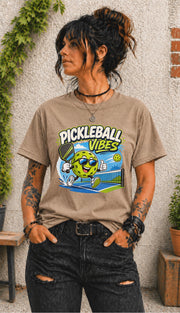 Woman wearing a Pickleball Vibes graphic t-shirt featuring a smiling pickleball character with sunglasses, paddle artwork, and colorful court-themed design.