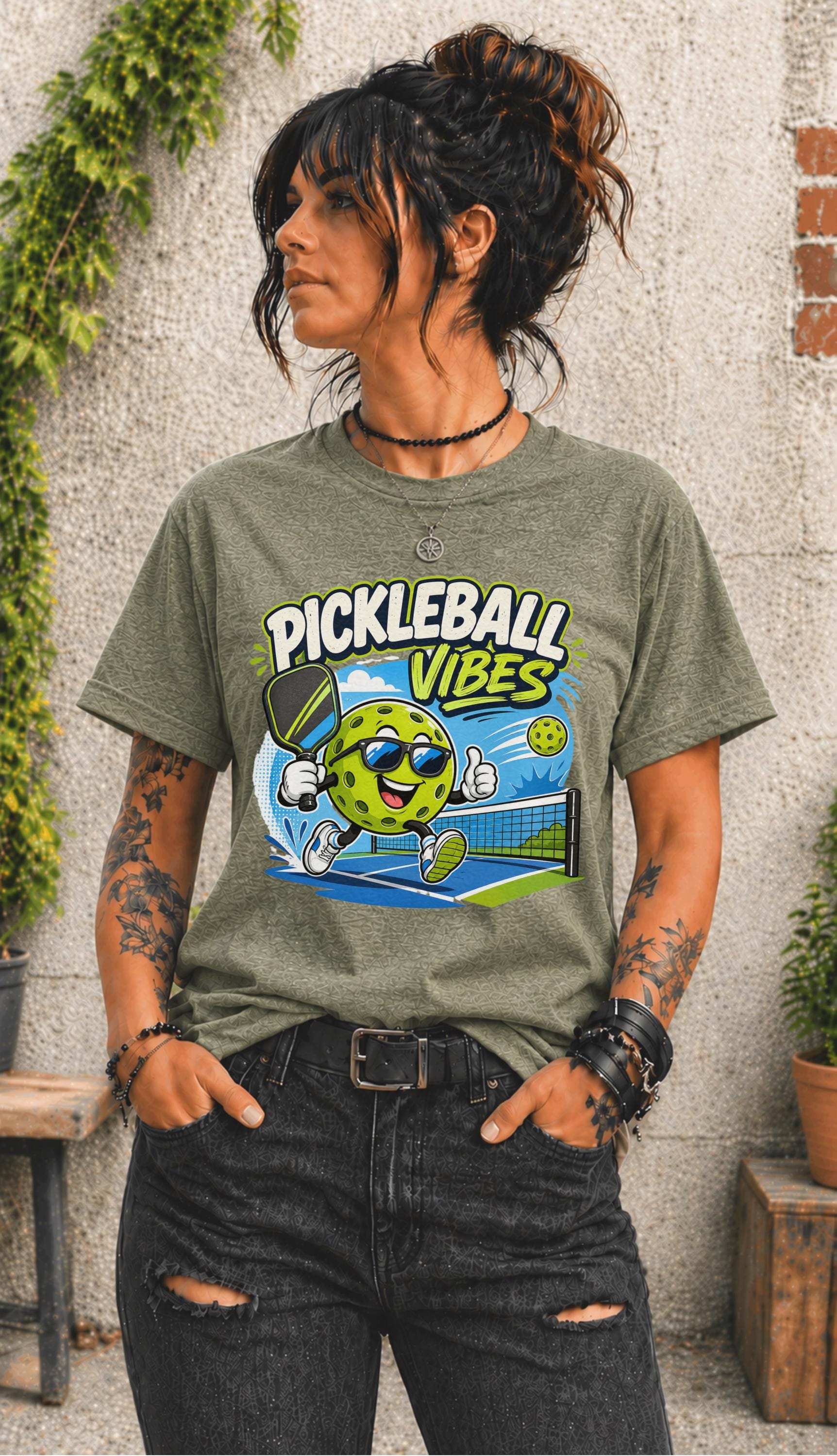 Woman wearing a Pickleball Vibes graphic t-shirt featuring a smiling pickleball character with sunglasses, paddle artwork, and colorful court-themed design.