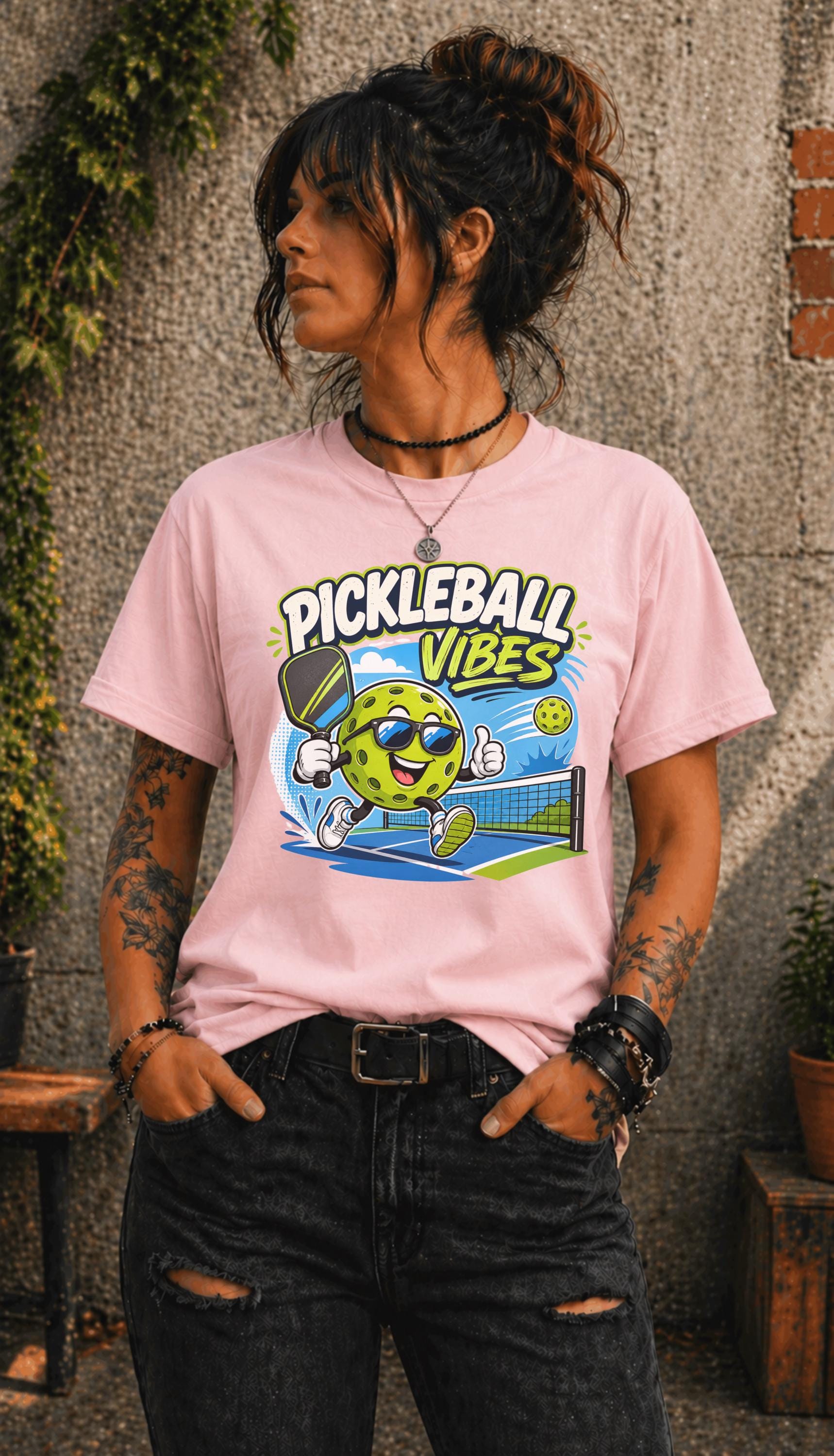 Woman wearing a Pickleball Vibes graphic t-shirt featuring a smiling pickleball character with sunglasses, paddle artwork, and colorful court-themed design.