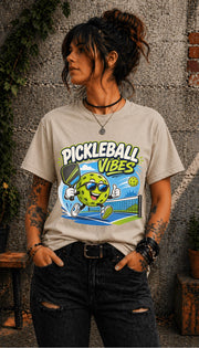 Woman wearing a Pickleball Vibes graphic t-shirt featuring a smiling pickleball character with sunglasses, paddle artwork, and colorful court-themed design.