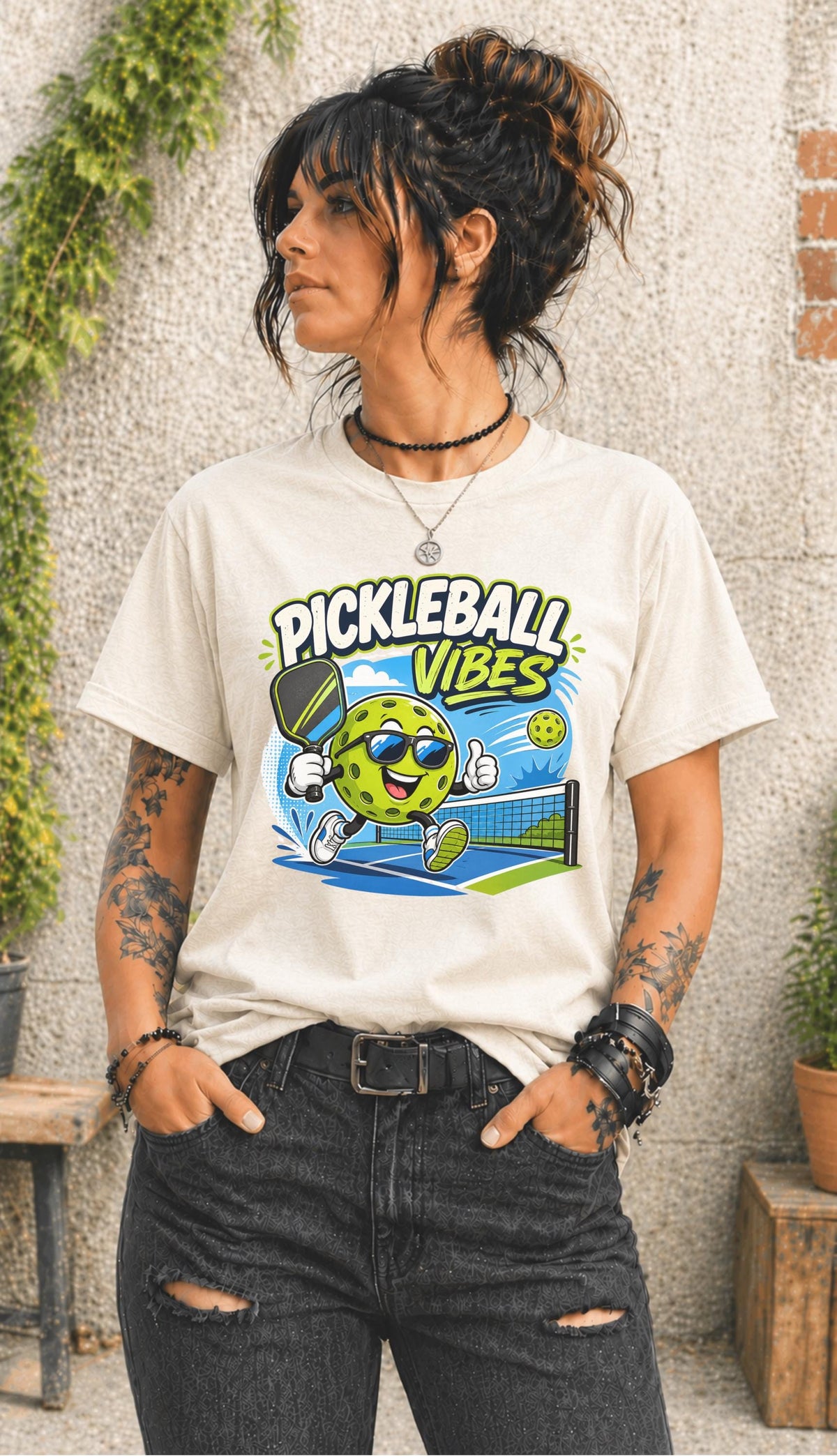 Woman wearing a Pickleball Vibes graphic t-shirt featuring a smiling pickleball character with sunglasses, paddle artwork, and colorful court-themed design.