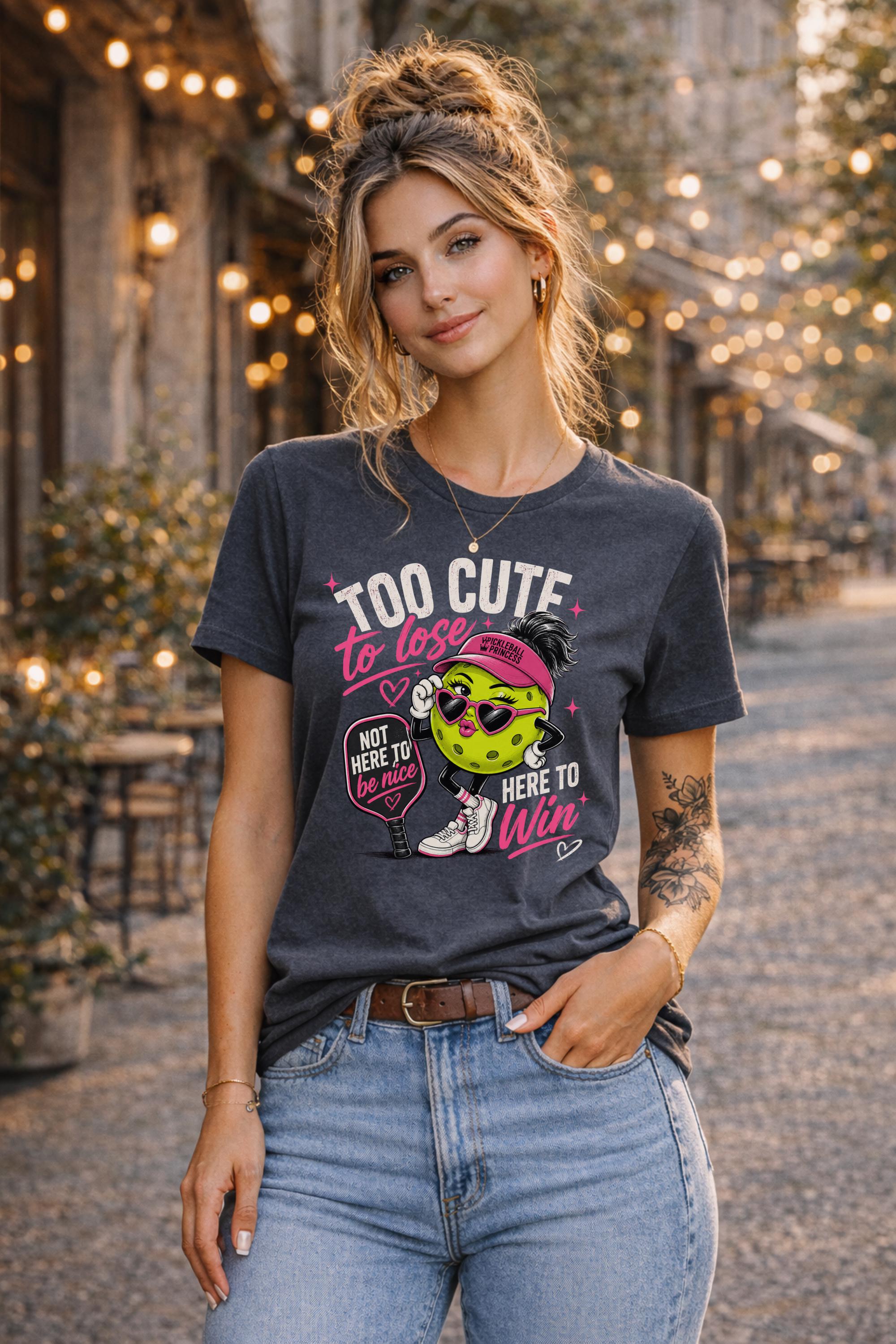 Woman wearing a Too Cute To Lose pickleball graphic t-shirt featuring a stylish pickleball character with heart sunglasses, pink visor, paddle artwork, and playful court-inspired design.