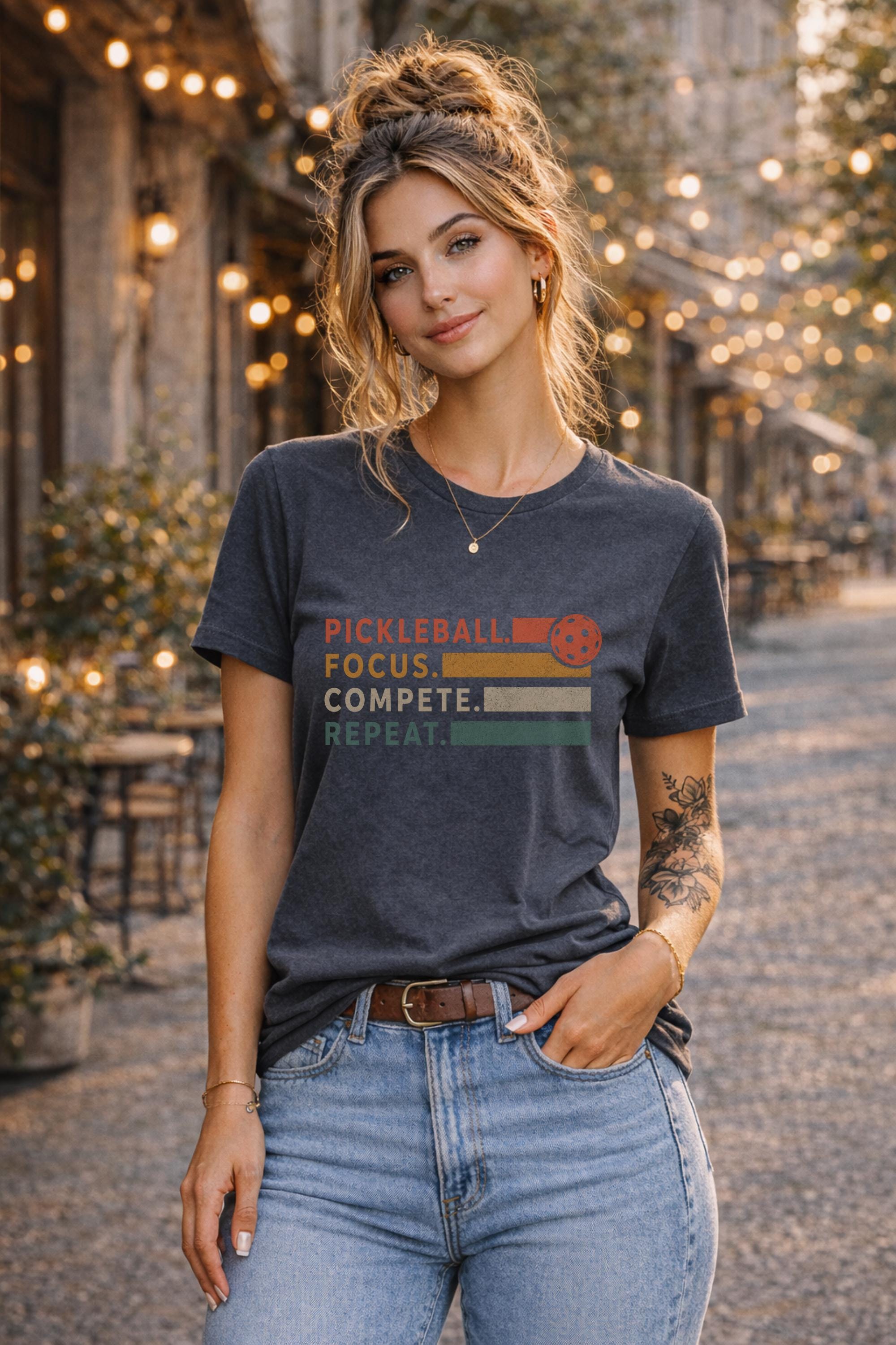 Woman wearing a graphic t-shirt featuring a vintage Pickleball Focus Compete Repeat design with retro stripes, pickleball icon, and motivational athletic typography.