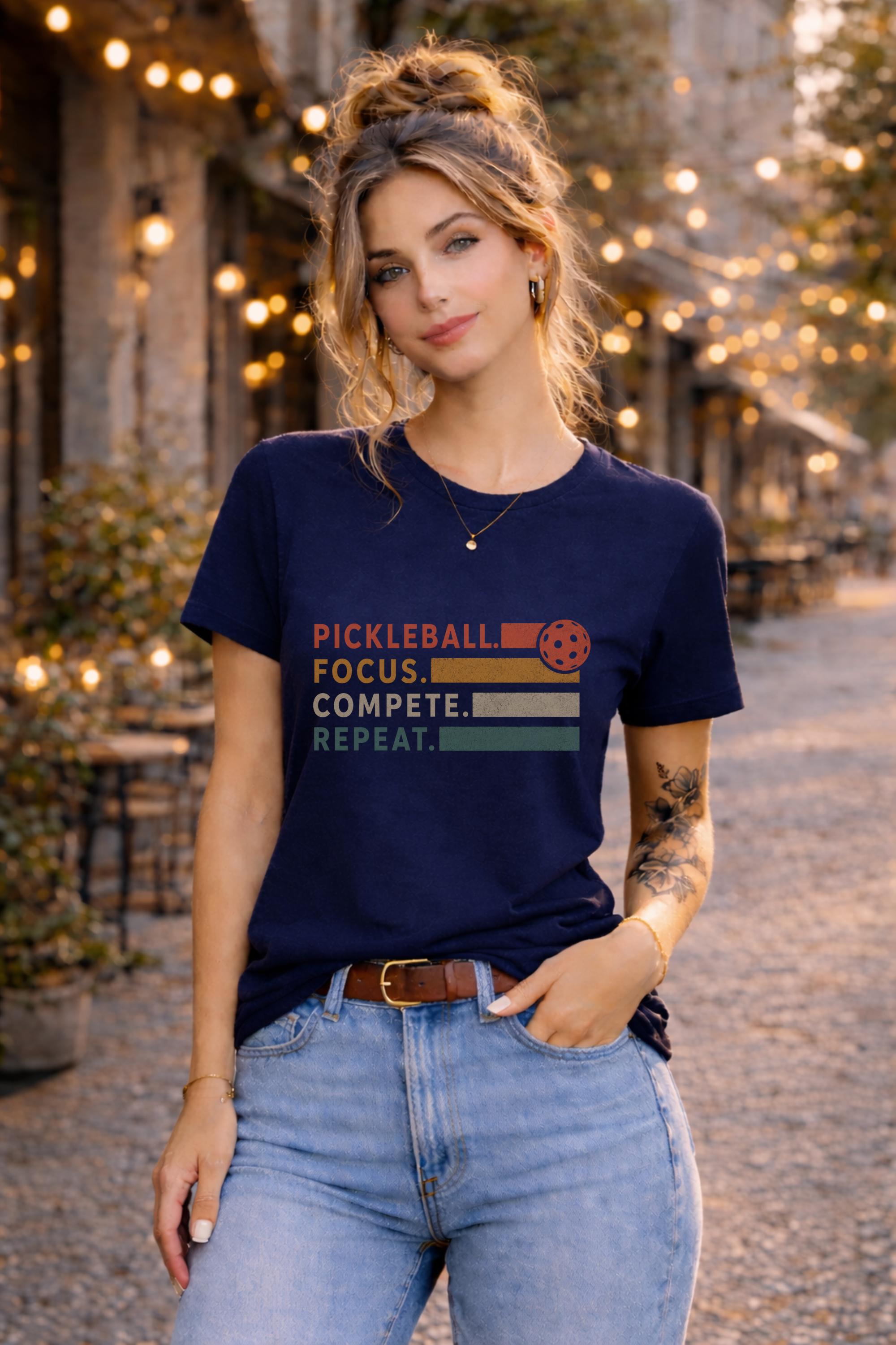 Woman wearing a graphic t-shirt featuring a vintage Pickleball Focus Compete Repeat design with retro stripes, pickleball icon, and motivational athletic typography.