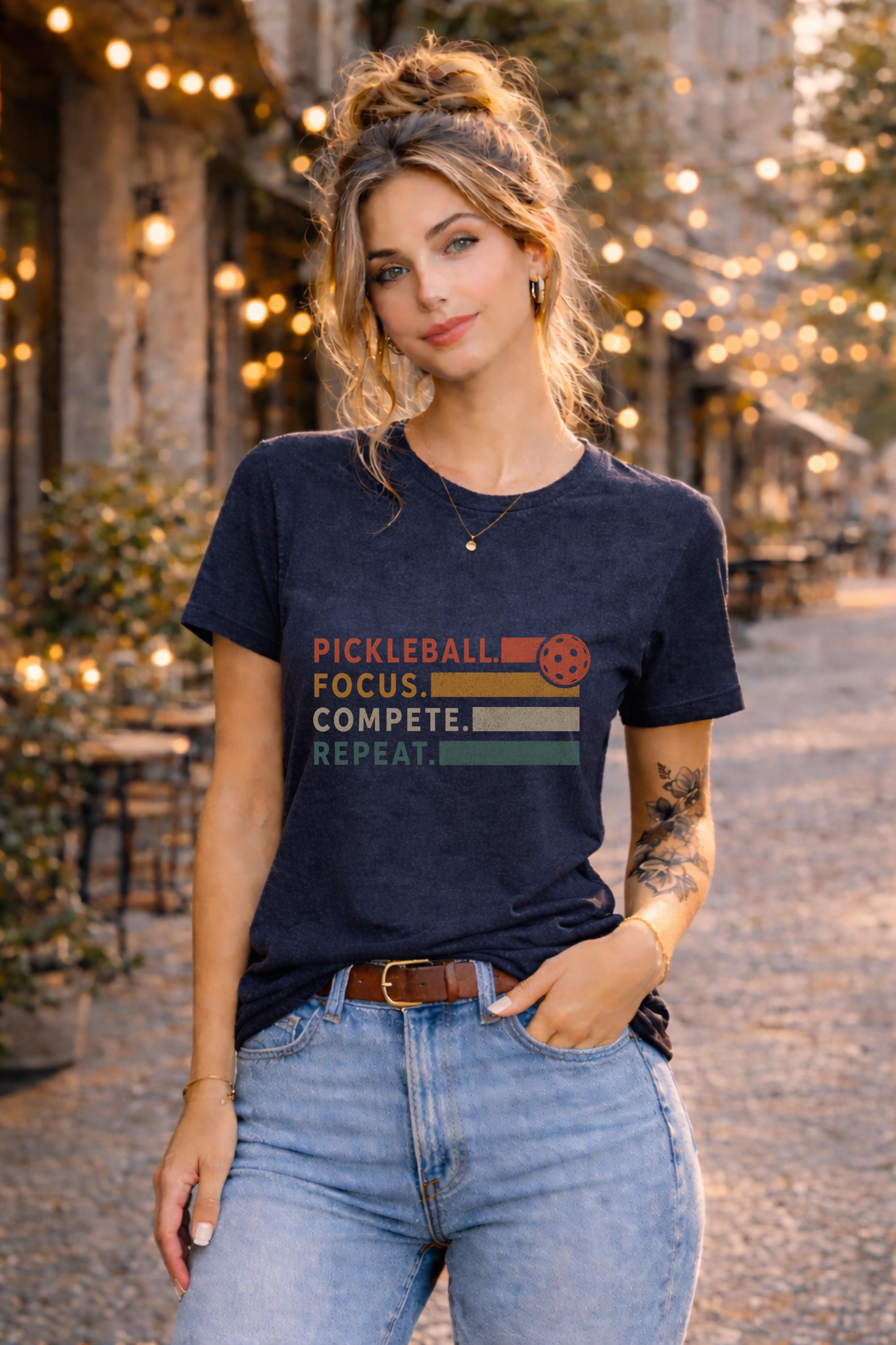 Woman wearing a graphic t-shirt featuring a vintage Pickleball Focus Compete Repeat design with retro stripes, pickleball icon, and motivational athletic typography.