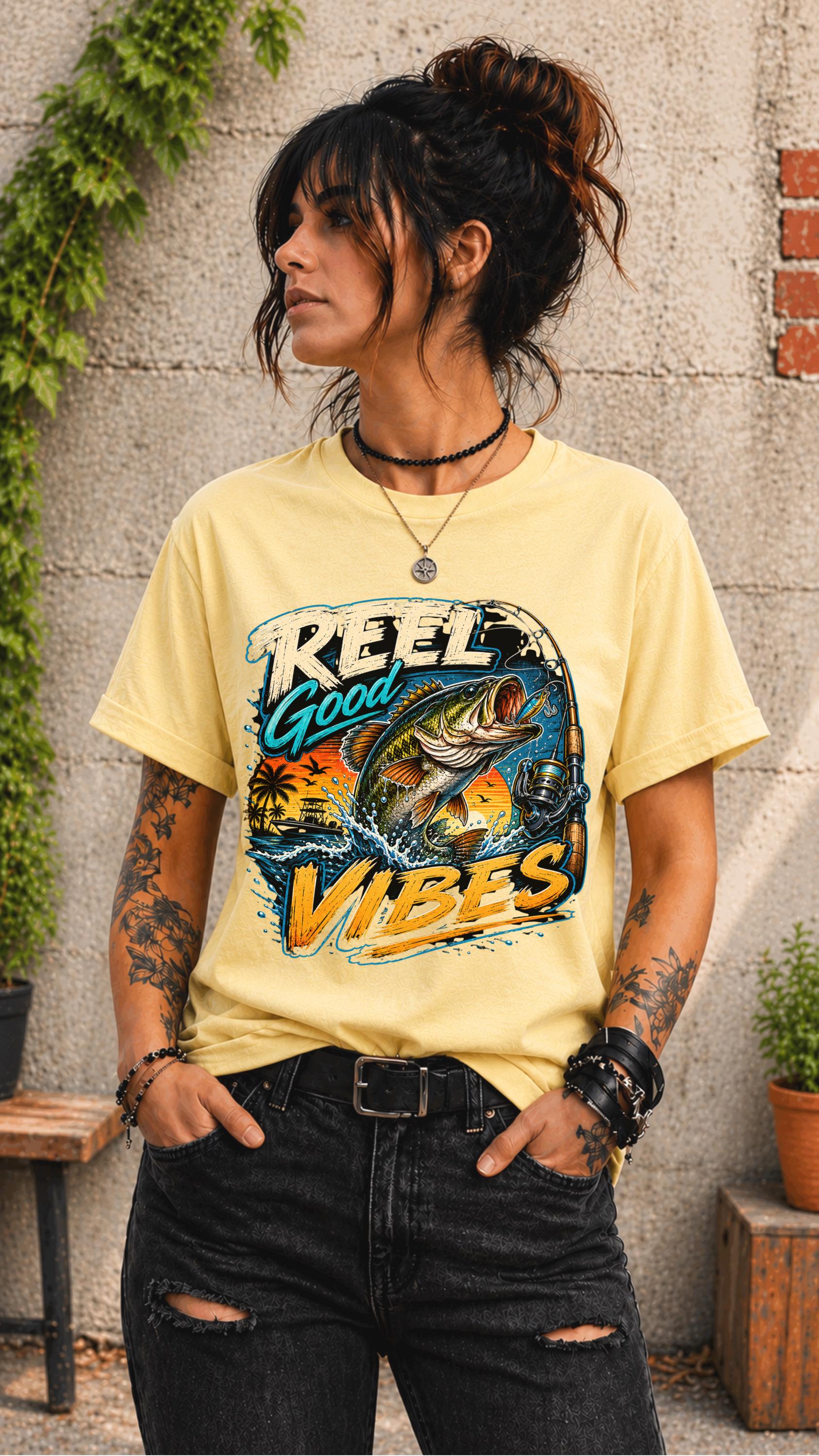 Woman wearing a graphic t-shirt featuring a jumping bass fish, fishing rod, tropical sunset scene, and Reel Good Vibes lettering.