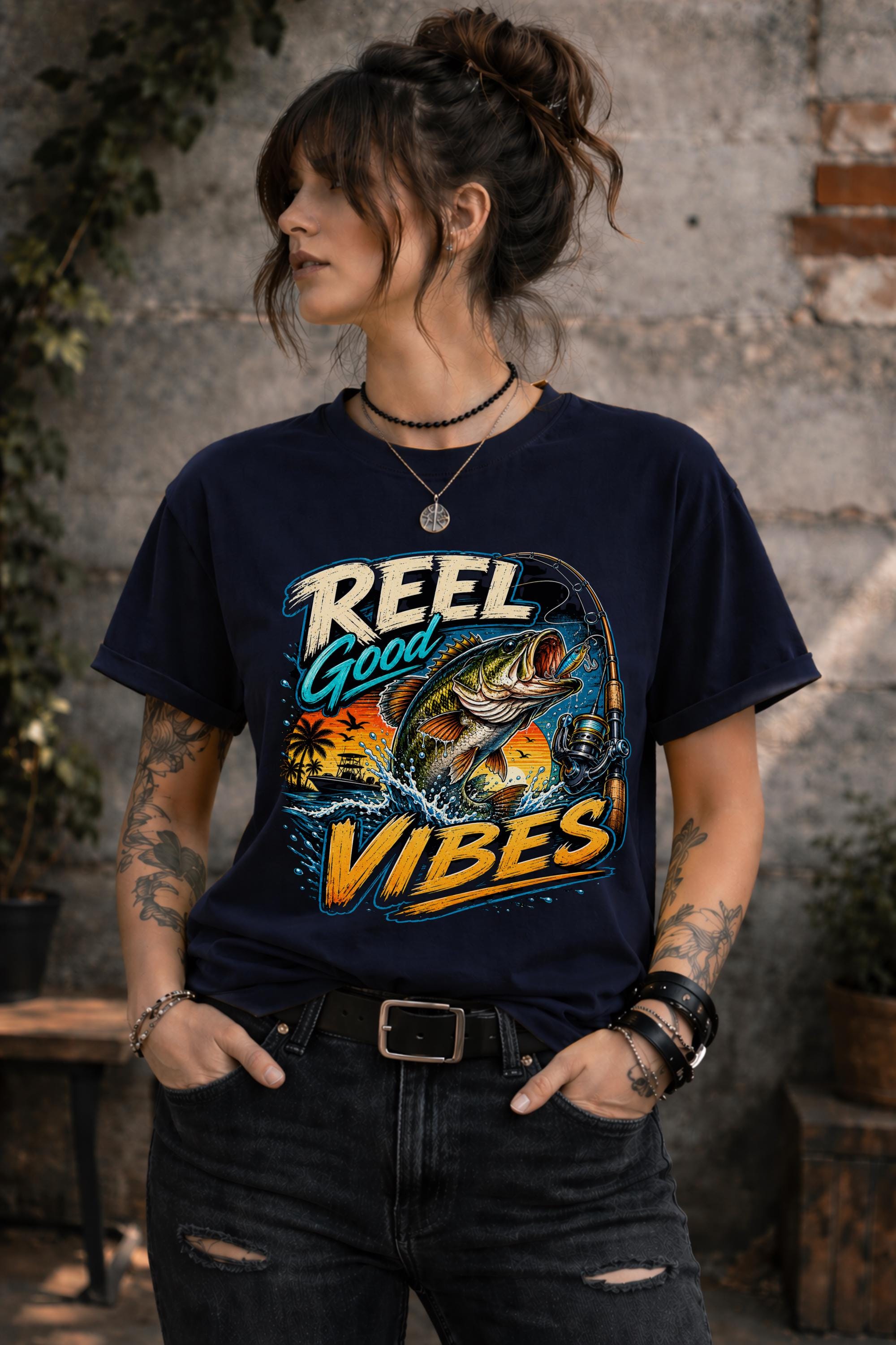 Woman wearing a graphic t-shirt featuring a jumping bass fish, fishing rod, tropical sunset scene, and Reel Good Vibes lettering.
