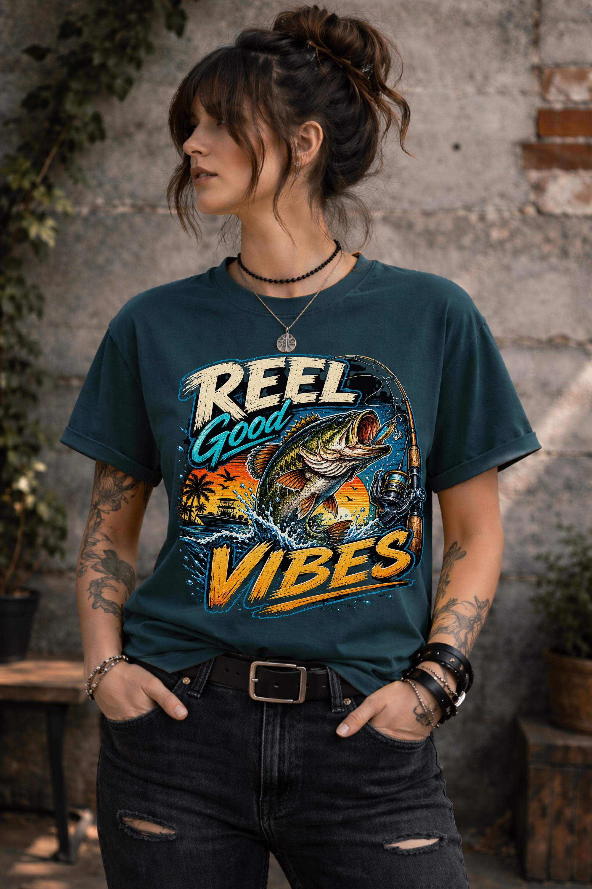 Woman wearing a graphic t-shirt featuring a jumping bass fish, fishing rod, tropical sunset scene, and Reel Good Vibes lettering.