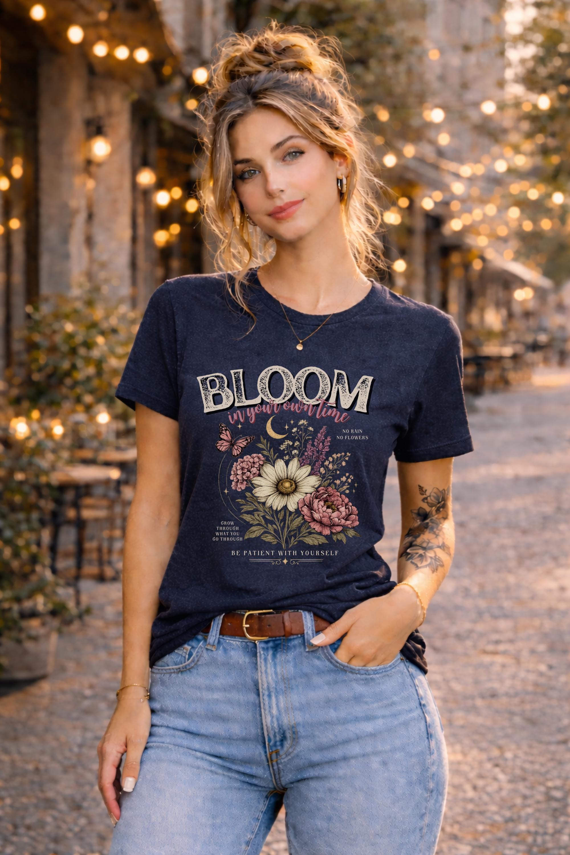 Woman wearing a floral inspirational t-shirt featuring the phrase "Bloom In Your Own Time" with vintage flowers, butterflies, moon accents, and self-love encouragement messages.