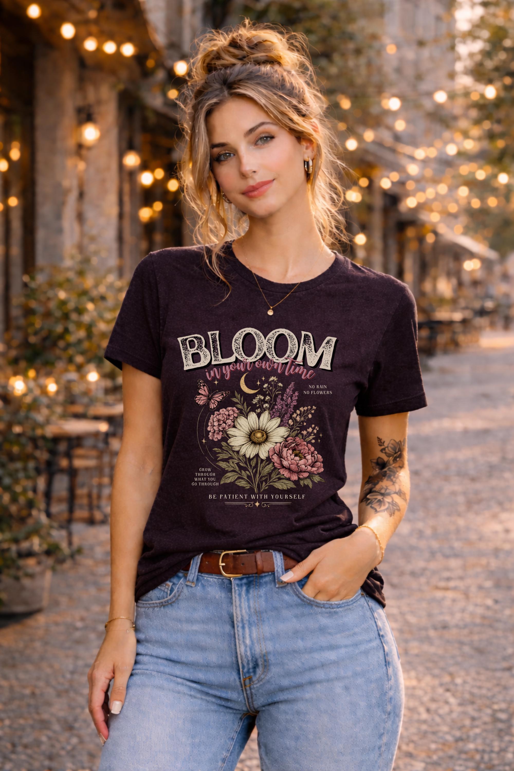 Woman wearing a floral inspirational t-shirt featuring the phrase "Bloom In Your Own Time" with vintage flowers, butterflies, moon accents, and self-love encouragement messages.
