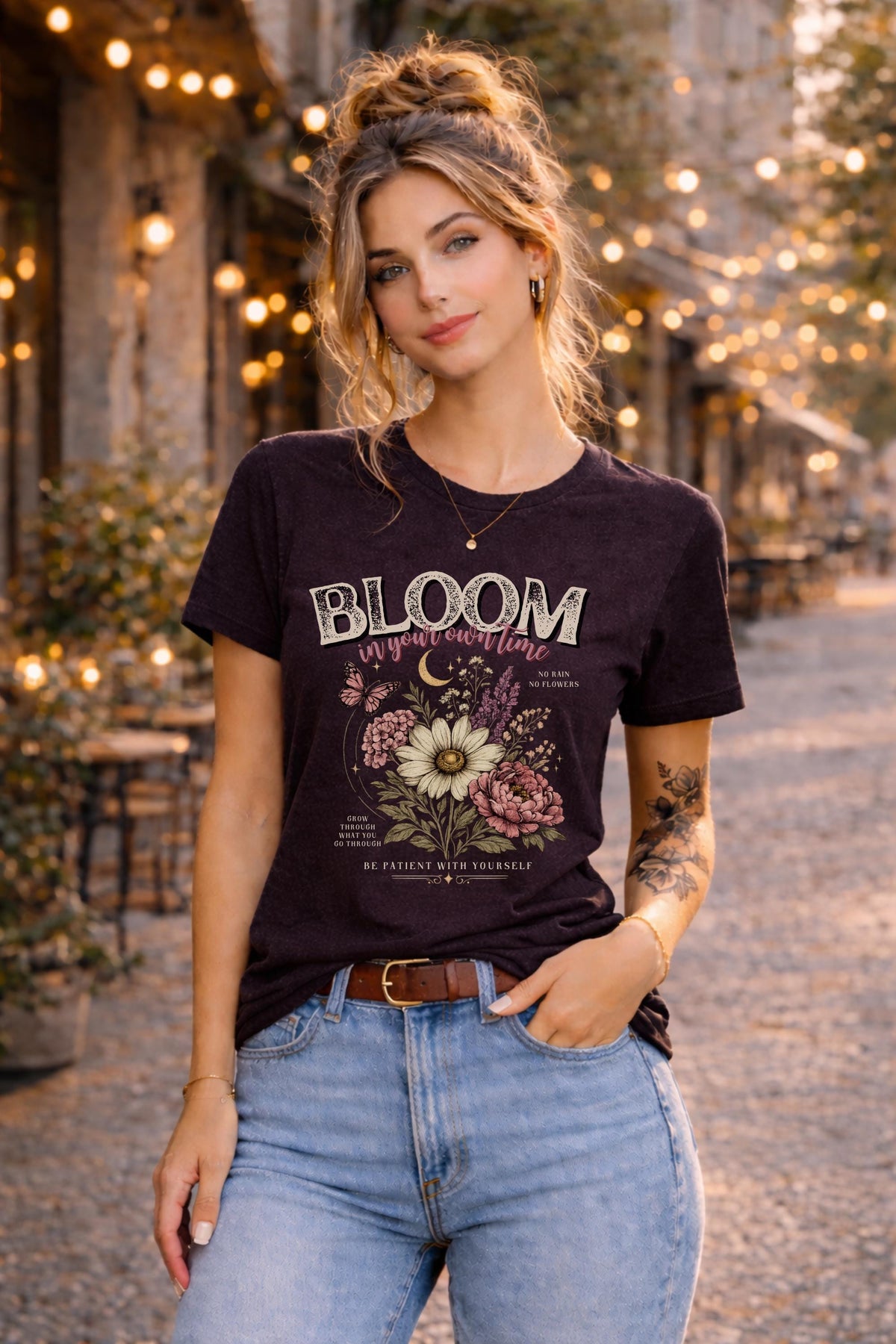 Woman wearing a floral inspirational t-shirt featuring the phrase "Bloom In Your Own Time" with vintage flowers, butterflies, moon accents, and self-love encouragement messages.