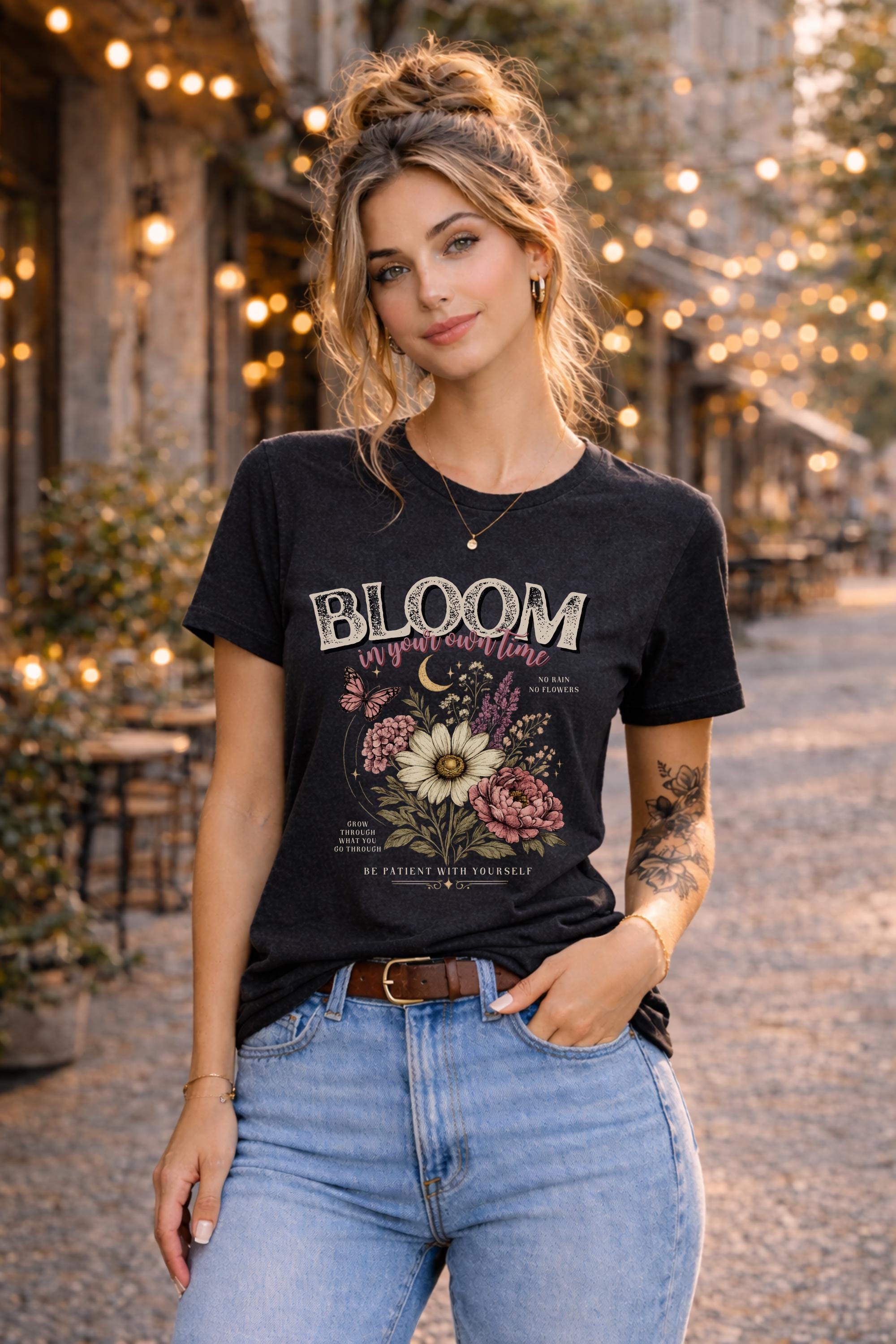 Woman wearing a floral inspirational t-shirt featuring the phrase "Bloom In Your Own Time" with vintage flowers, butterflies, moon accents, and self-love encouragement messages.