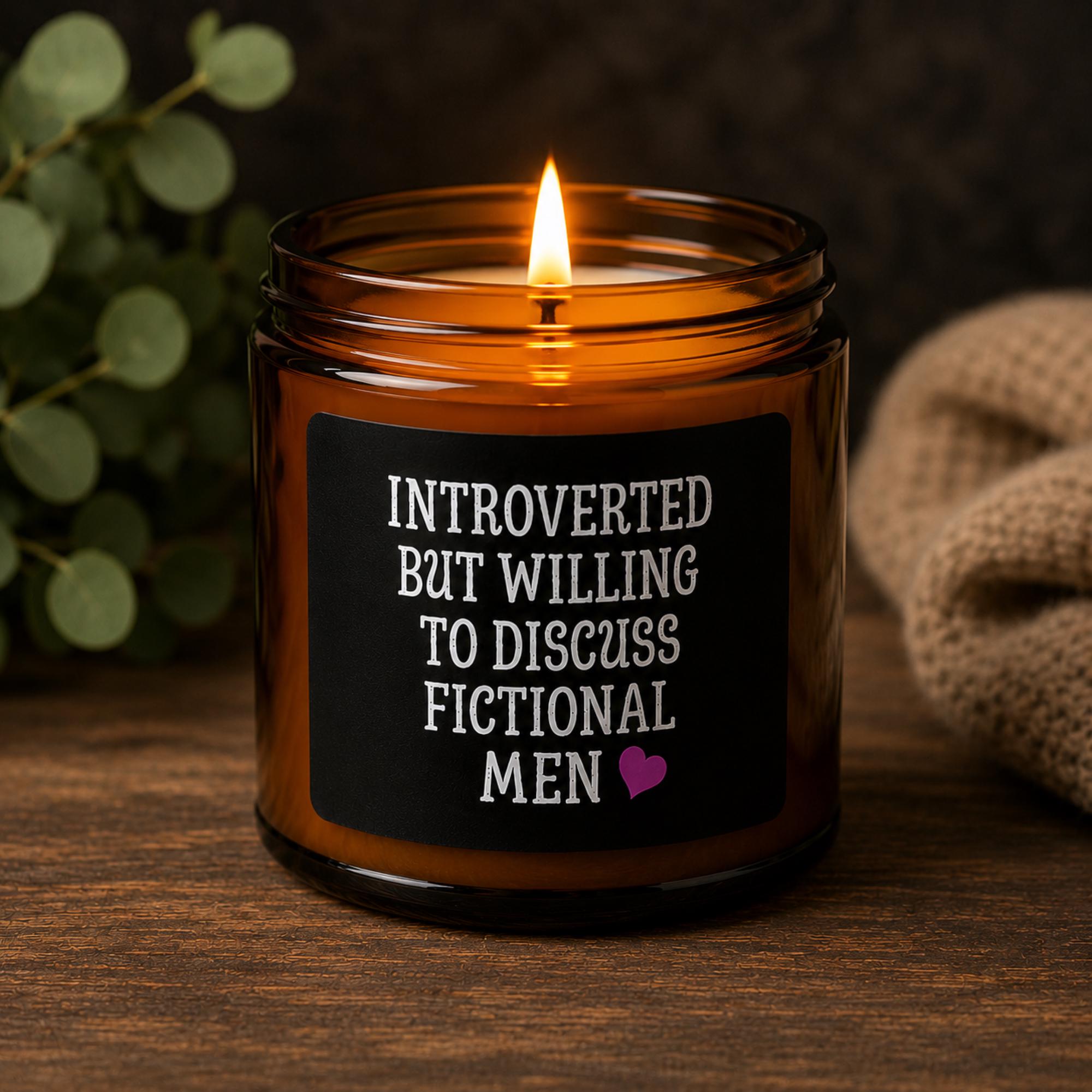 Dark romance themed scented soy candles featuring the phrase "Introverted But Willing To Discuss Fictional Men" displayed alongside gothic books and candlelit decor.