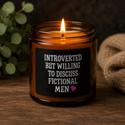Dark romance themed scented soy candles featuring the phrase "Introverted But Willing To Discuss Fictional Men" displayed alongside gothic books and candlelit decor.