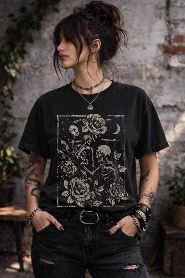 Woman wearing a black graphic t-shirt featuring two skeleton lovers surrounded by roses beneath a crescent moon in a gothic dark academia style design.