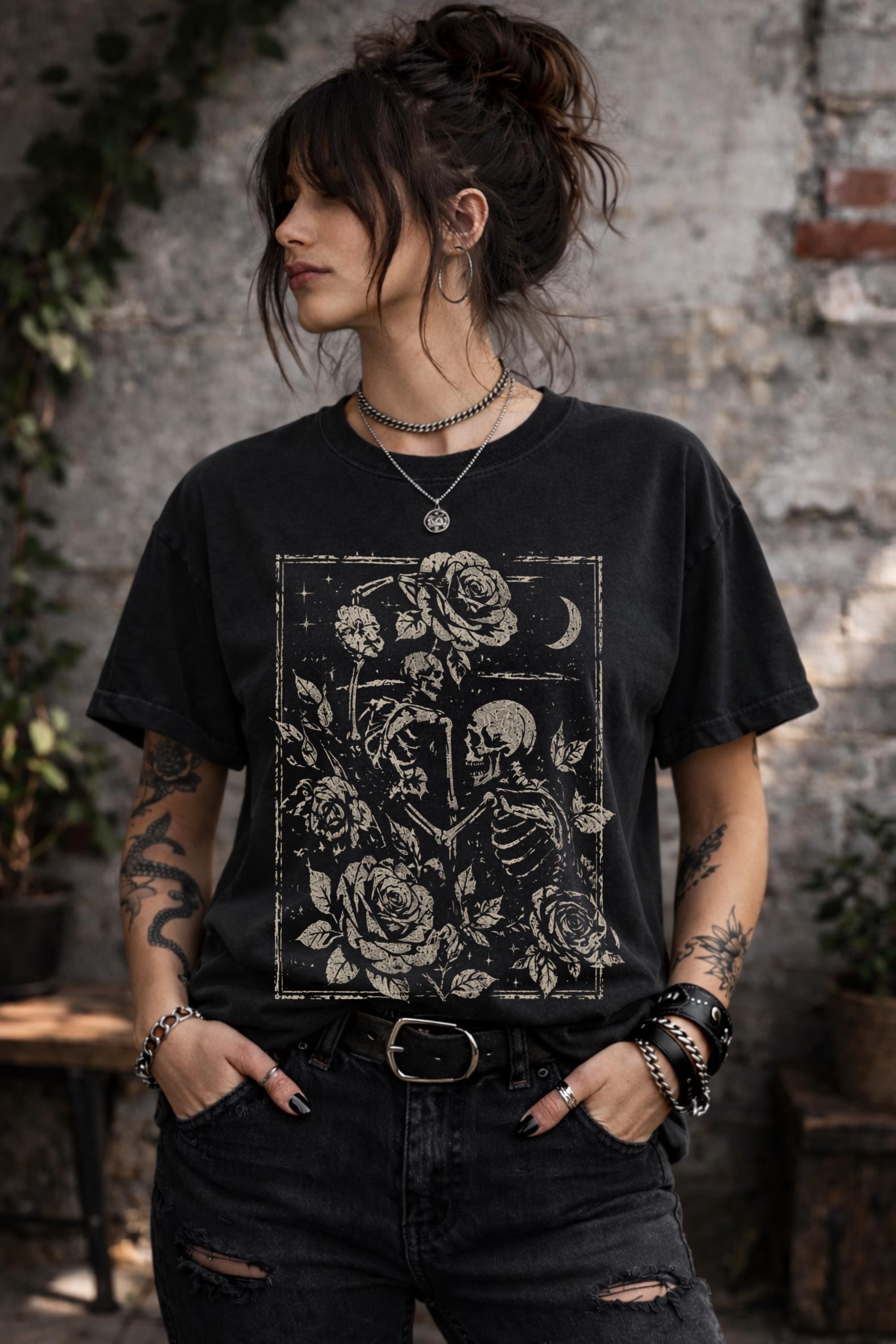 Woman wearing a black graphic t-shirt featuring two skeleton lovers surrounded by roses beneath a crescent moon in a gothic dark academia style design.