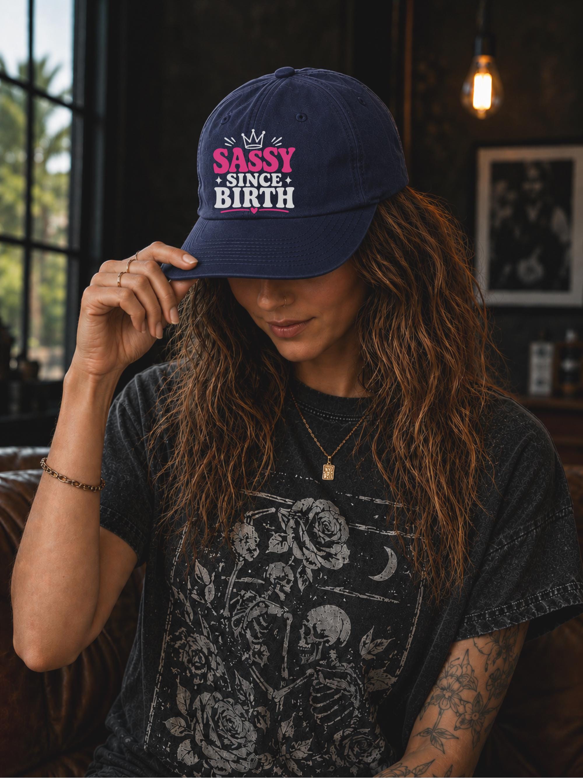 Classic dad cap featuring a pink and white "Sassy Since Birth" graphic with crown artwork, styled in a casual fashion setting.