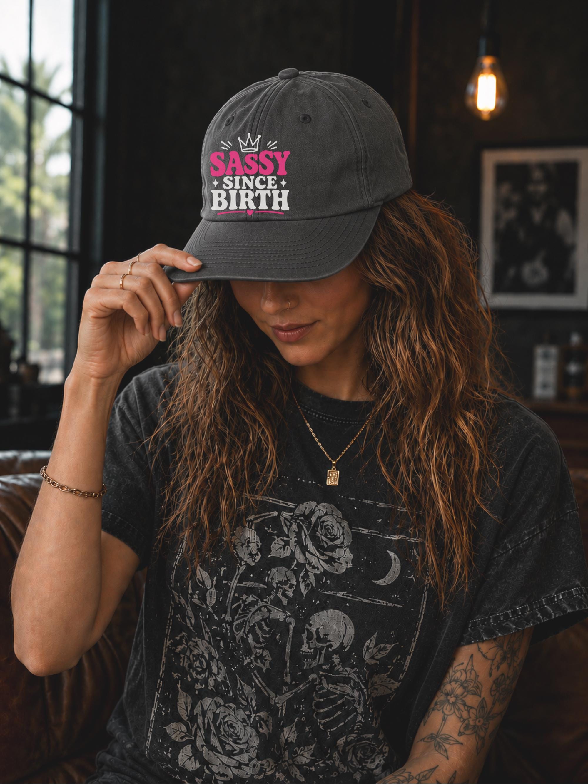 Classic dad cap featuring a pink and white "Sassy Since Birth" graphic with crown artwork, styled in a casual fashion setting.