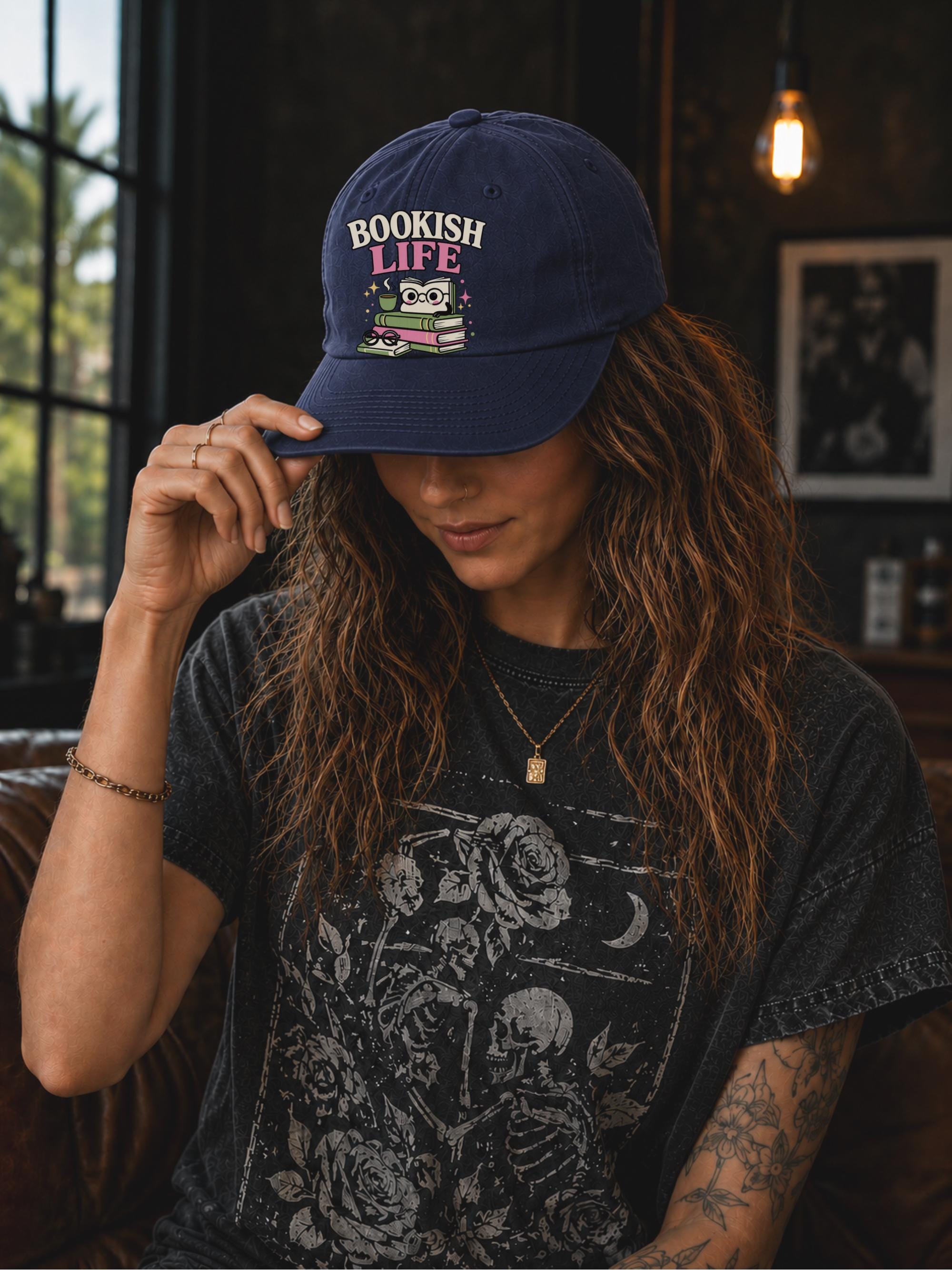 Woman wearing a navy classic dad cap featuring a colorful Bookish Life graphic with stacked books, glasses, and a playful reading-themed illustration.
