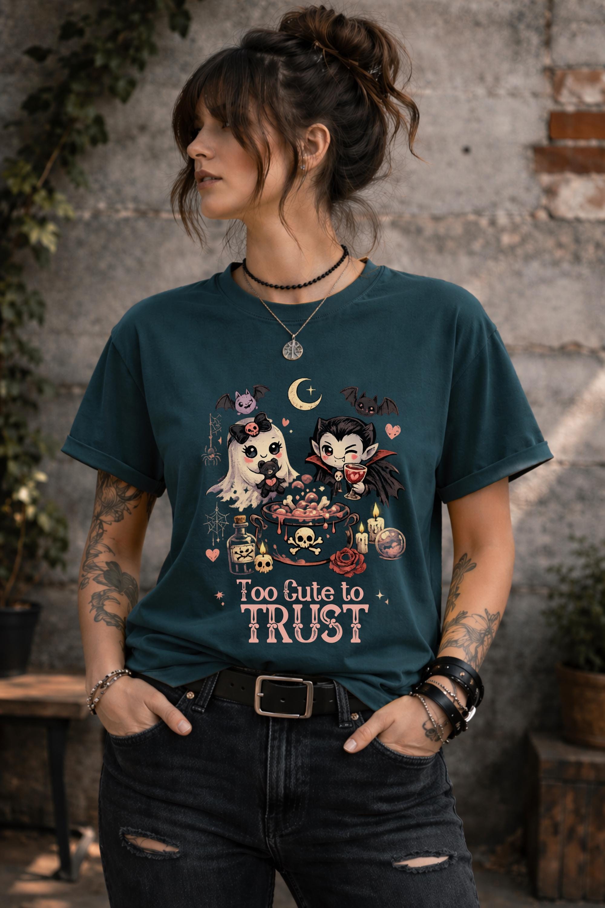 Gothic Halloween tee displaying Too Cute To Trust design with bats, roses, candles, skulls, potion bottles, and moon accents.