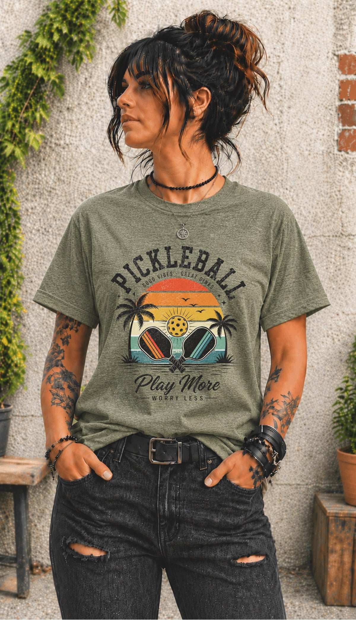 Woman wearing a Pickleball Play More Worry Less graphic t-shirt featuring retro paddles, tropical palm trees, vintage sunset artwork, and coastal-inspired pickleball design.