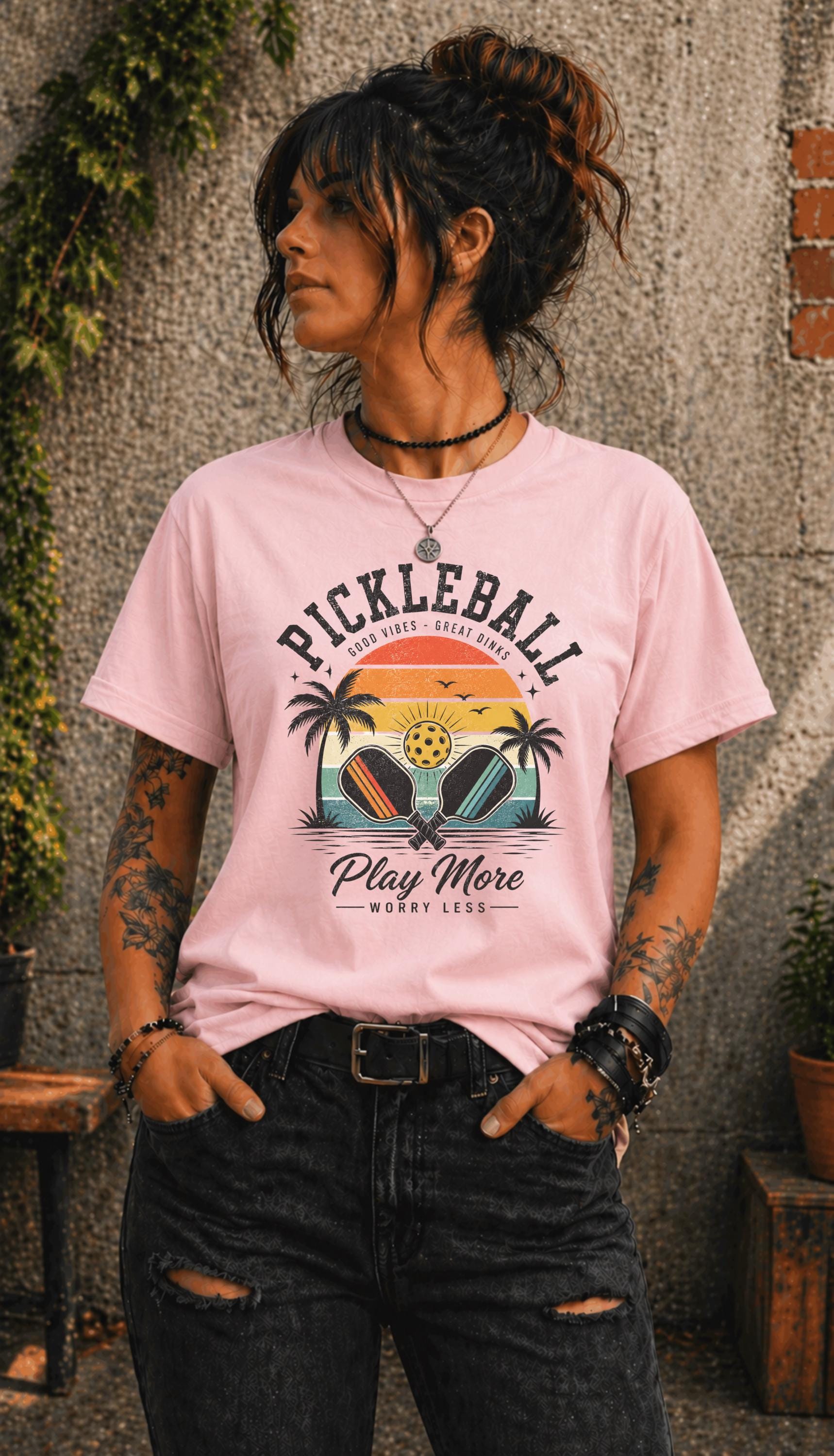 Woman wearing a Pickleball Play More Worry Less graphic t-shirt featuring retro paddles, tropical palm trees, vintage sunset artwork, and coastal-inspired pickleball design.