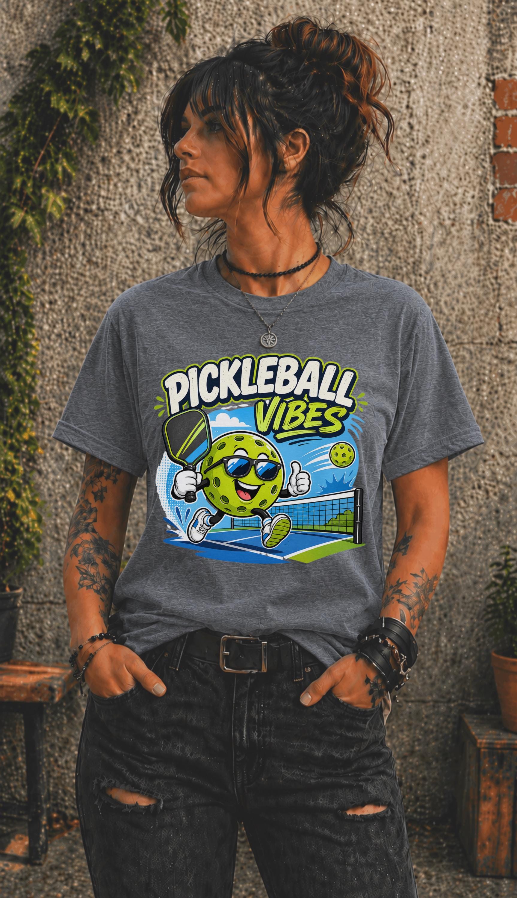 Woman wearing a Pickleball Vibes graphic t-shirt featuring a smiling pickleball character with sunglasses, paddle artwork, and colorful court-themed design.
