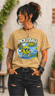 Woman wearing a Pickleball Vibes graphic t-shirt featuring a smiling pickleball character with sunglasses, paddle artwork, and colorful court-themed design.