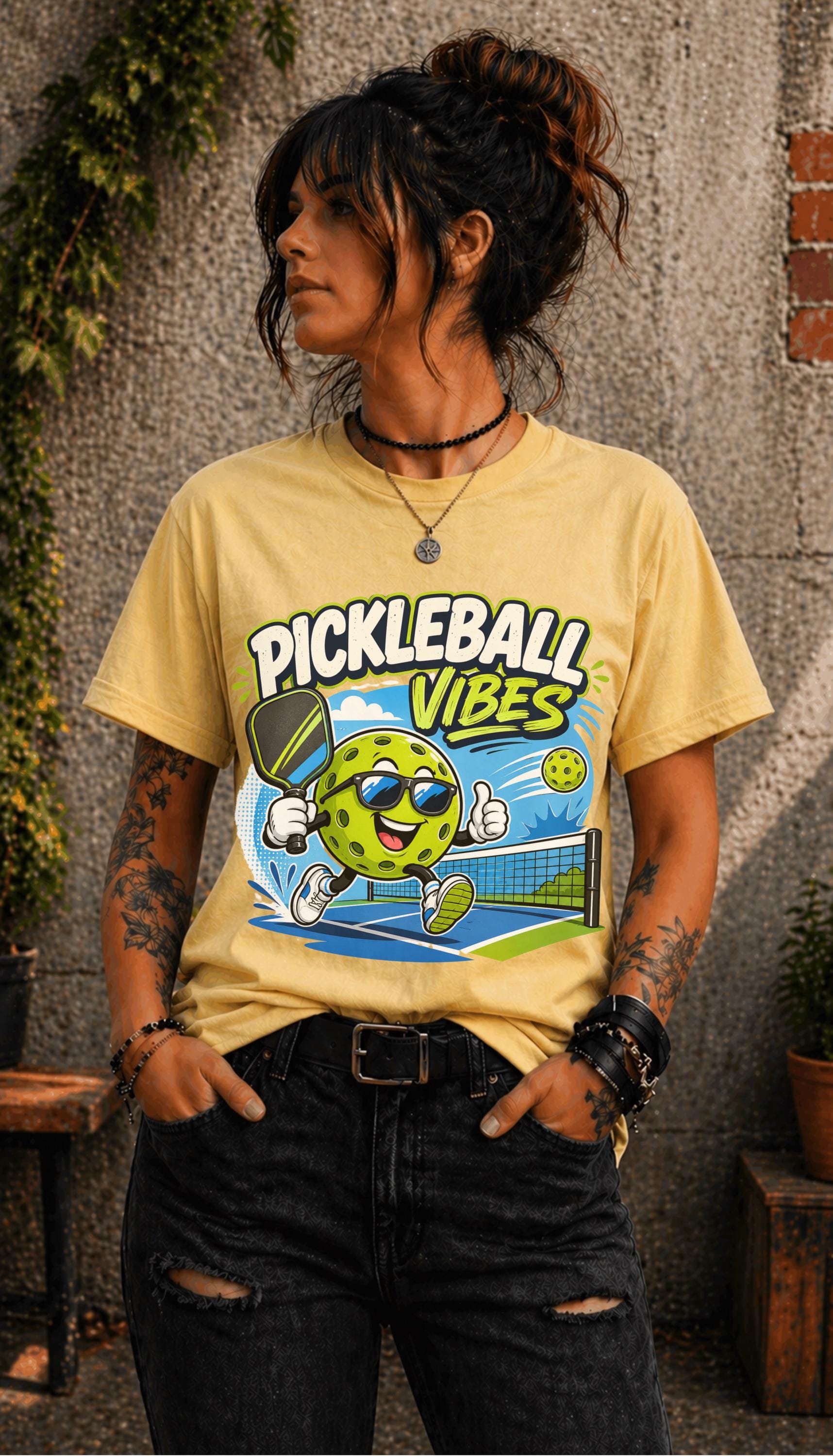 Woman wearing a Pickleball Vibes graphic t-shirt featuring a smiling pickleball character with sunglasses, paddle artwork, and colorful court-themed design.