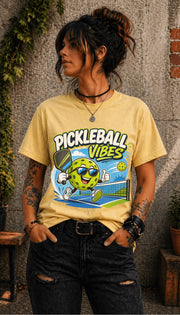 Woman wearing a Pickleball Vibes graphic t-shirt featuring a smiling pickleball character with sunglasses, paddle artwork, and colorful court-themed design.